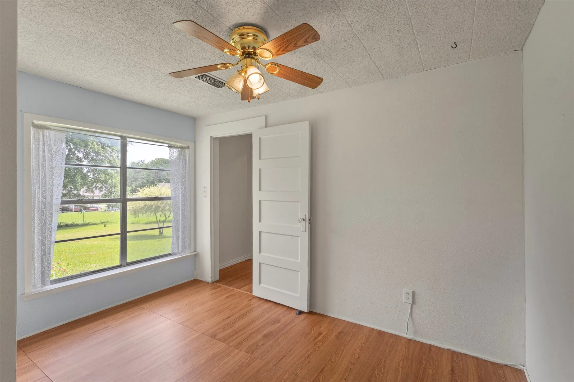 Bright interior room featuring wood-finish flooring, a ceiling fan with light fixture, and a large window overlooking a grassy exterior