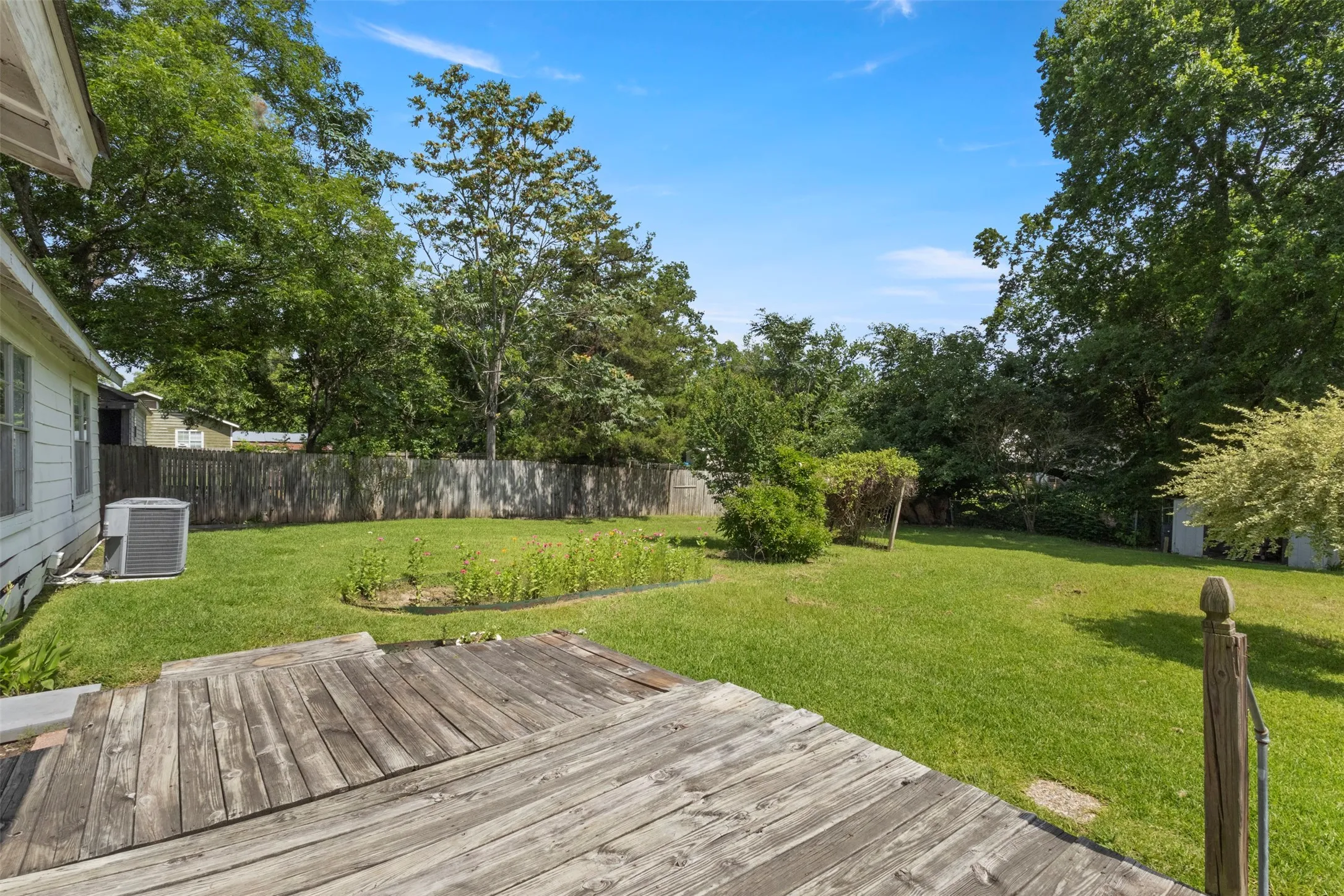 Expansive backyard featuring a natural wood deck, established privacy fencing, a manicured lawn, and mature trees