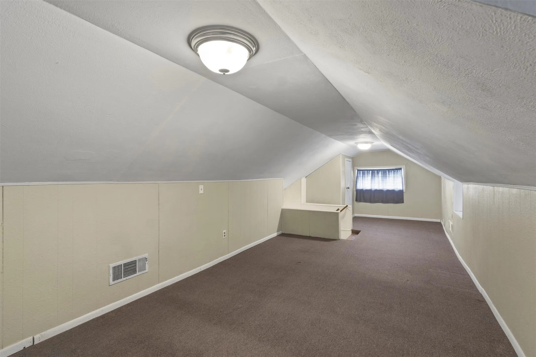Carpeted room with sloped ceilings and light beige paneling