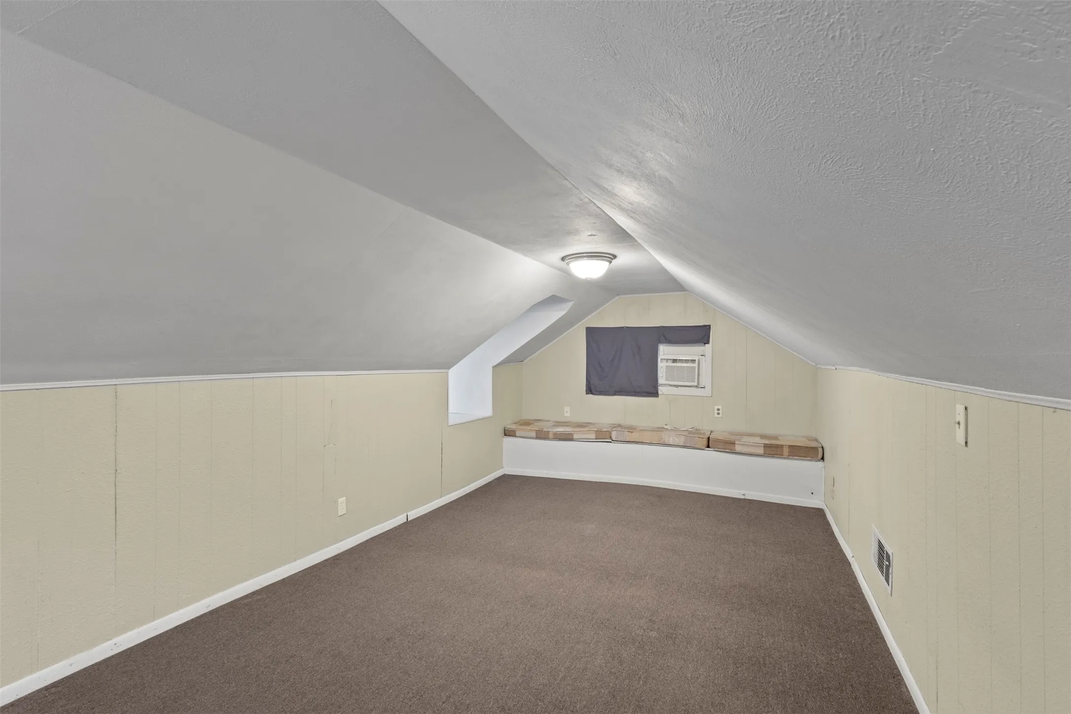 Attic space featuring sloped ceilings, paneling, and brown carpet flooring