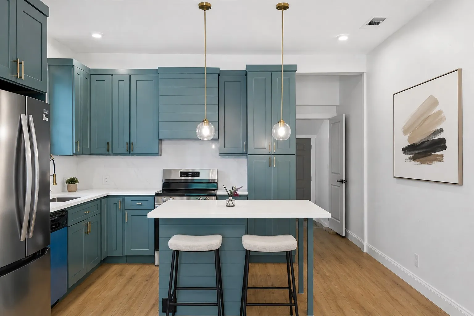 Kitchen featuring wood-finish flooring, two-tone cabinetry with gold-finish hardware, stainless steel appliances, white countertops, and a central island with pendant lighting
