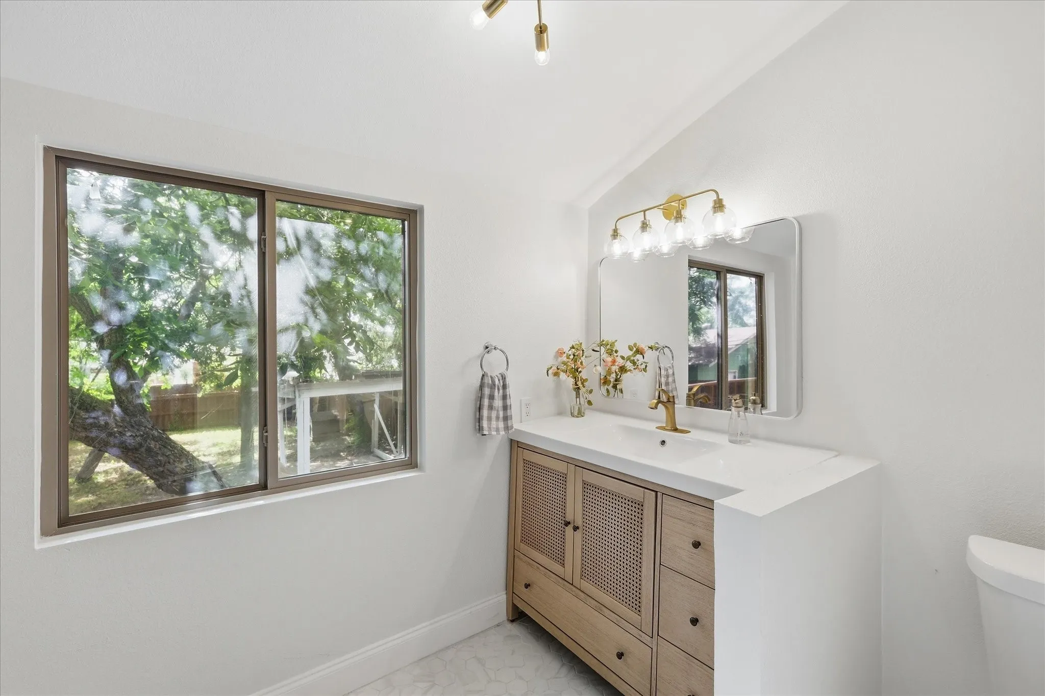 Bathroom featuring a light wood-finish vanity with woven paneling, a white countertop with an integrated sink, and a modern gold-tone faucet