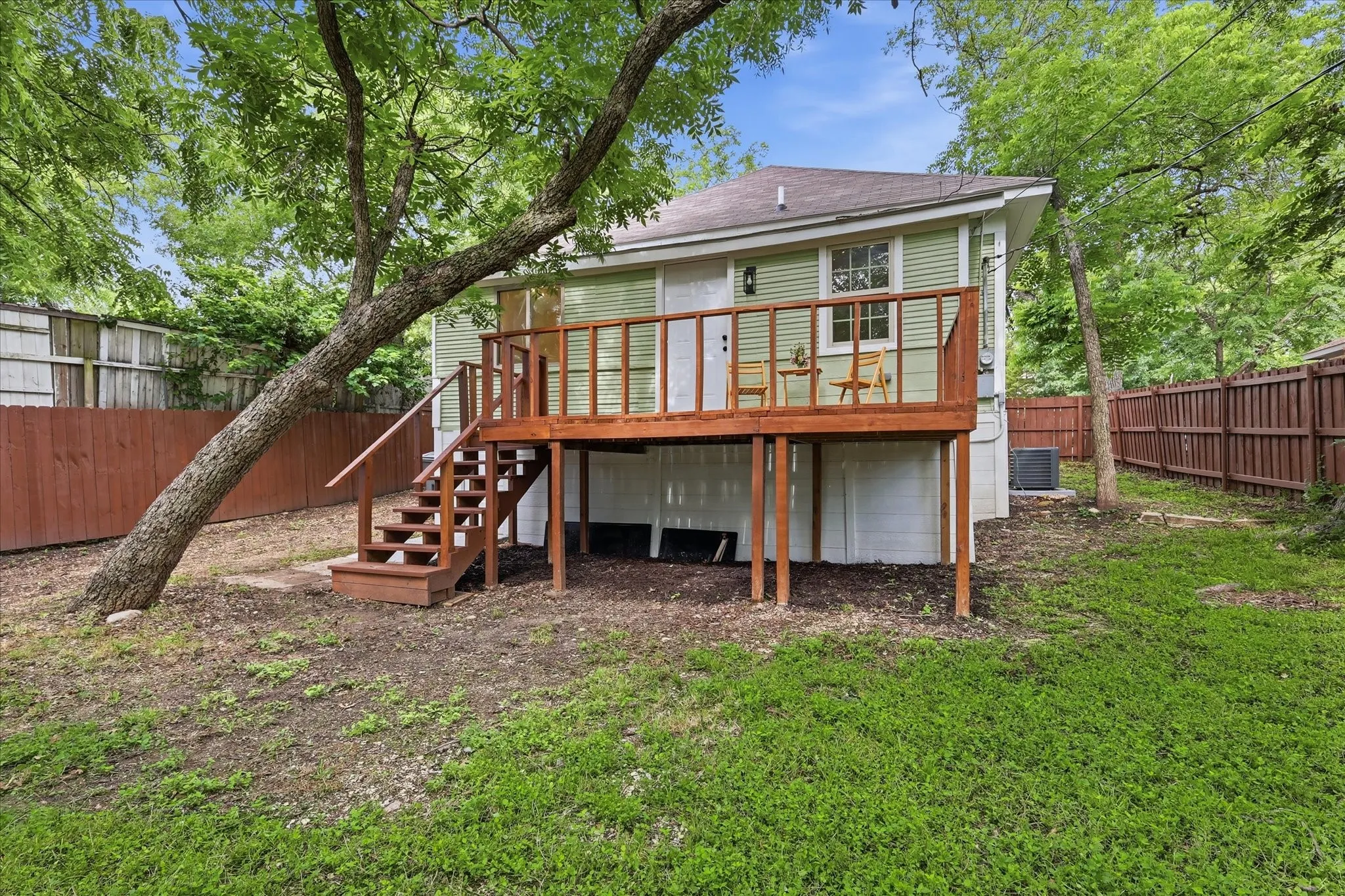 Rear exterior featuring a raised wood deck with railing and stairs, light green siding, and a partially fenced yard