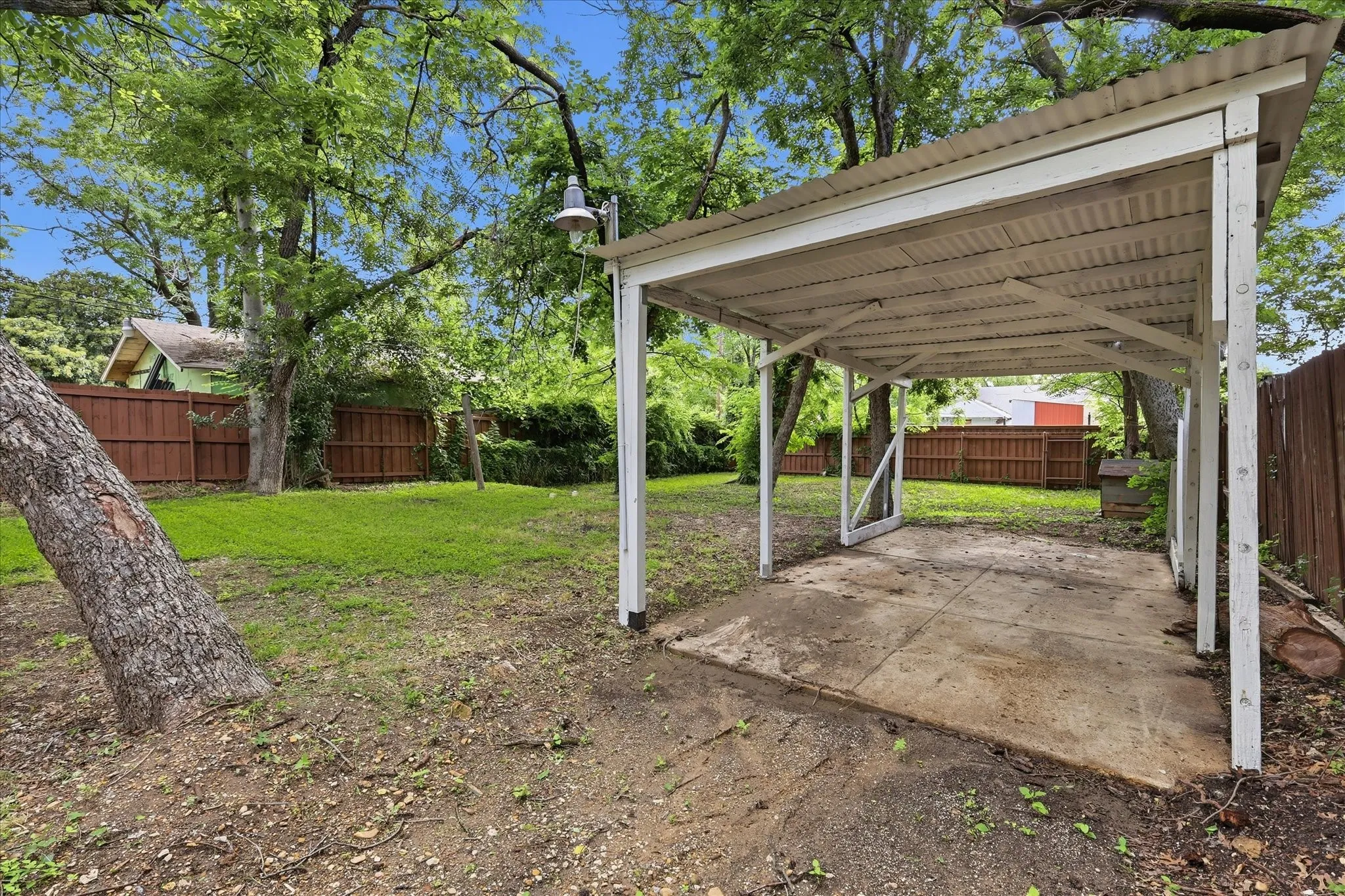 Carport with a corrugated metal roof and concrete pad, set within a fenced yard