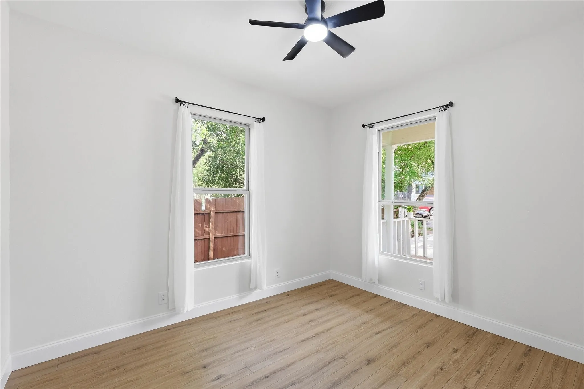 Room featuring wood-finish flooring, crisp white walls, and a ceiling fan with integrated lighting