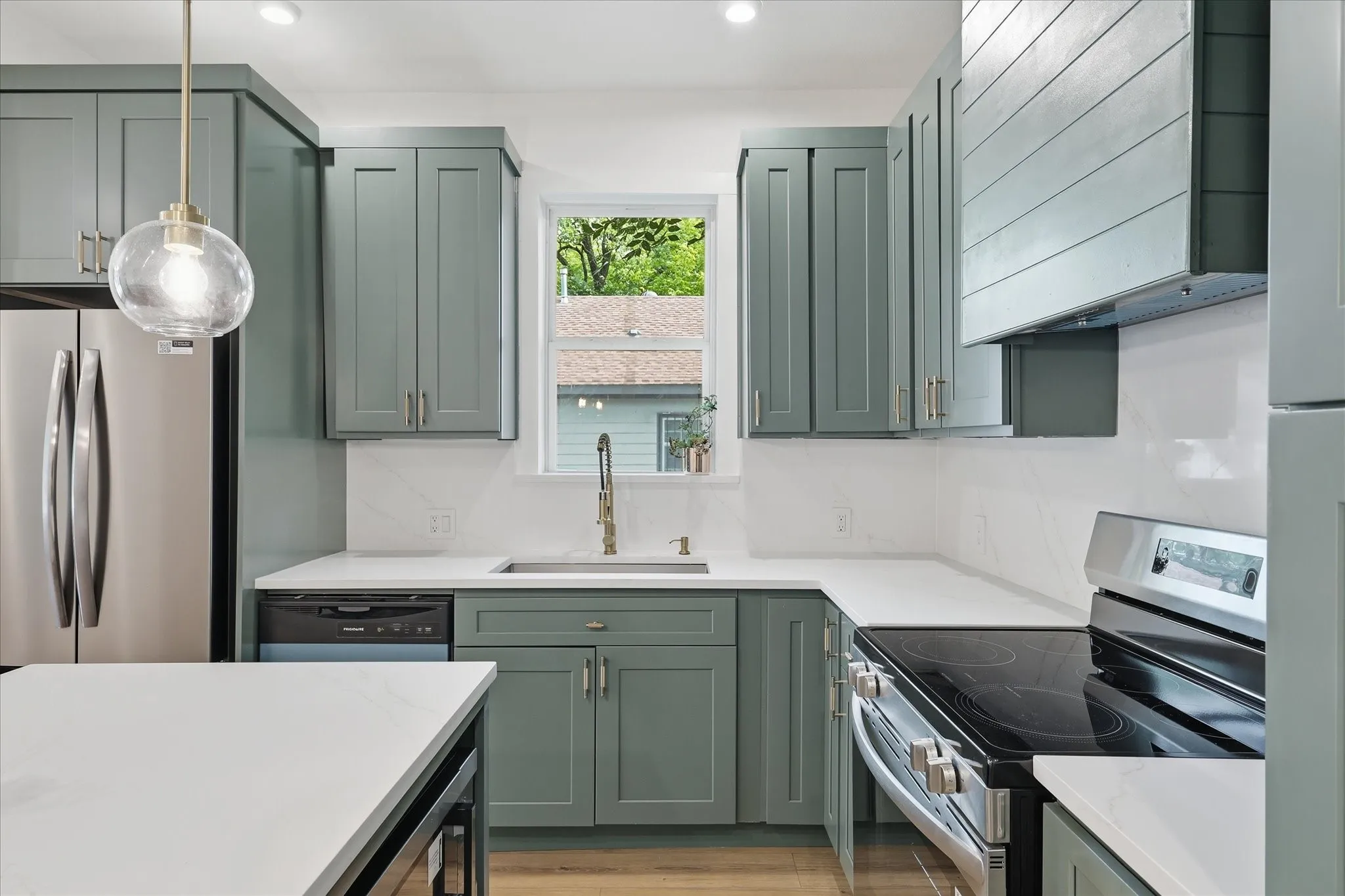 Modern kitchen featuring sage green shaker cabinetry, stainless steel appliances, white countertops, and a full-height tile backsplash