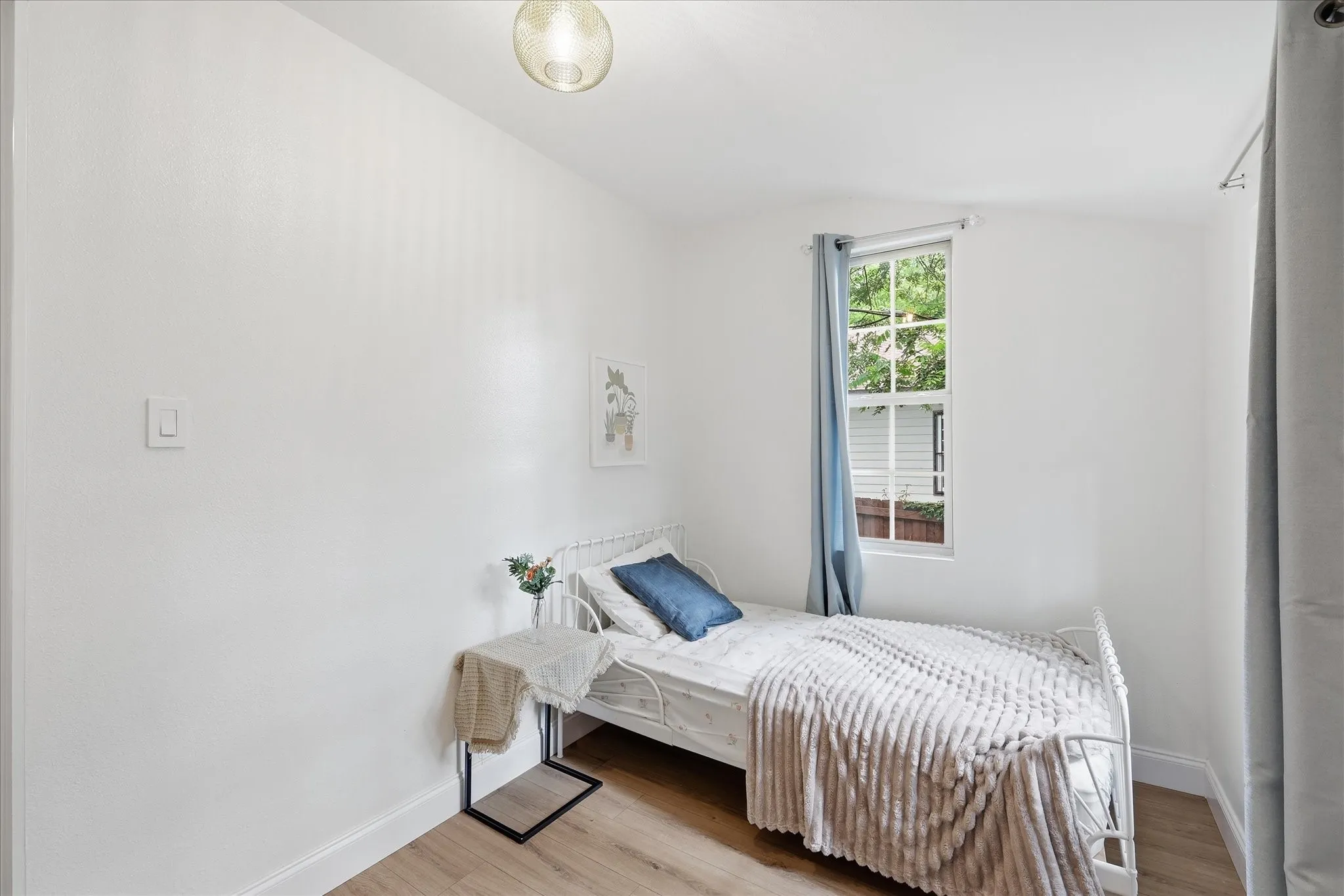 Bedroom featuring wood-finish flooring, white baseboards, a single window with white framing, and a ceiling-mounted light fixture