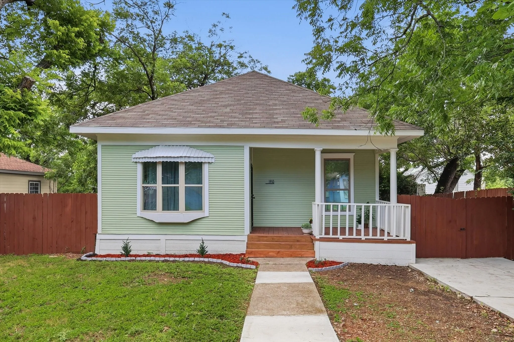 Light green exterior with white trim, featuring a covered porch with white railings and a bay window with an awning
