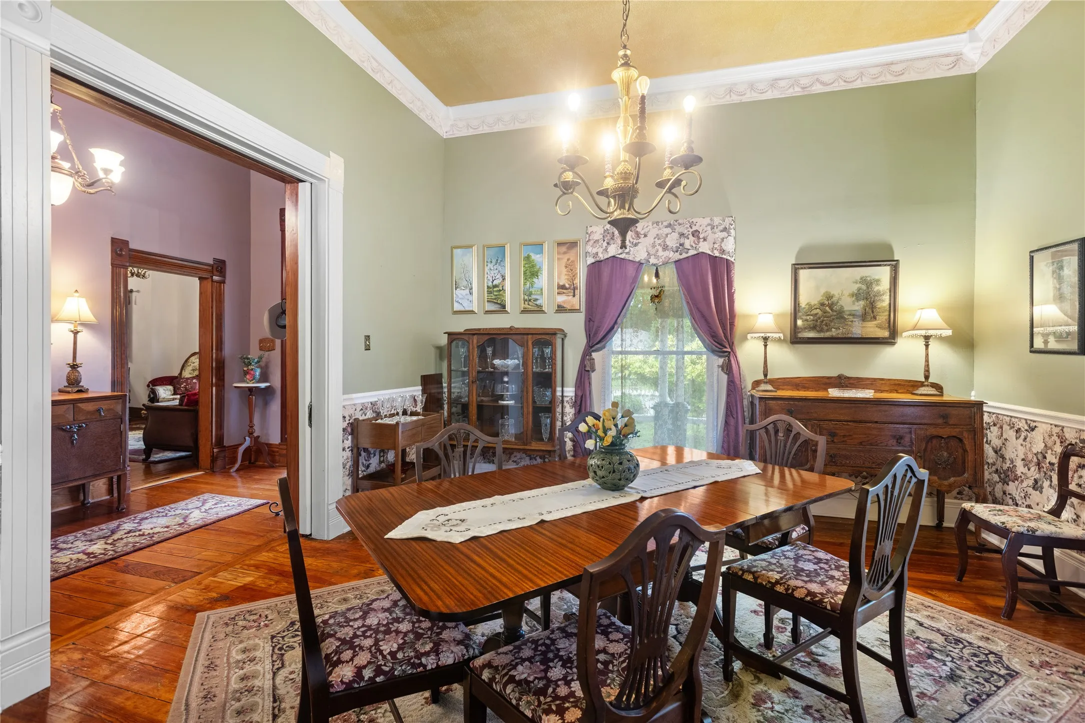 Formal dining area featuring hardwood flooring, detailed crown molding, a decorative chandelier, wainscoting, and large window with exterior light