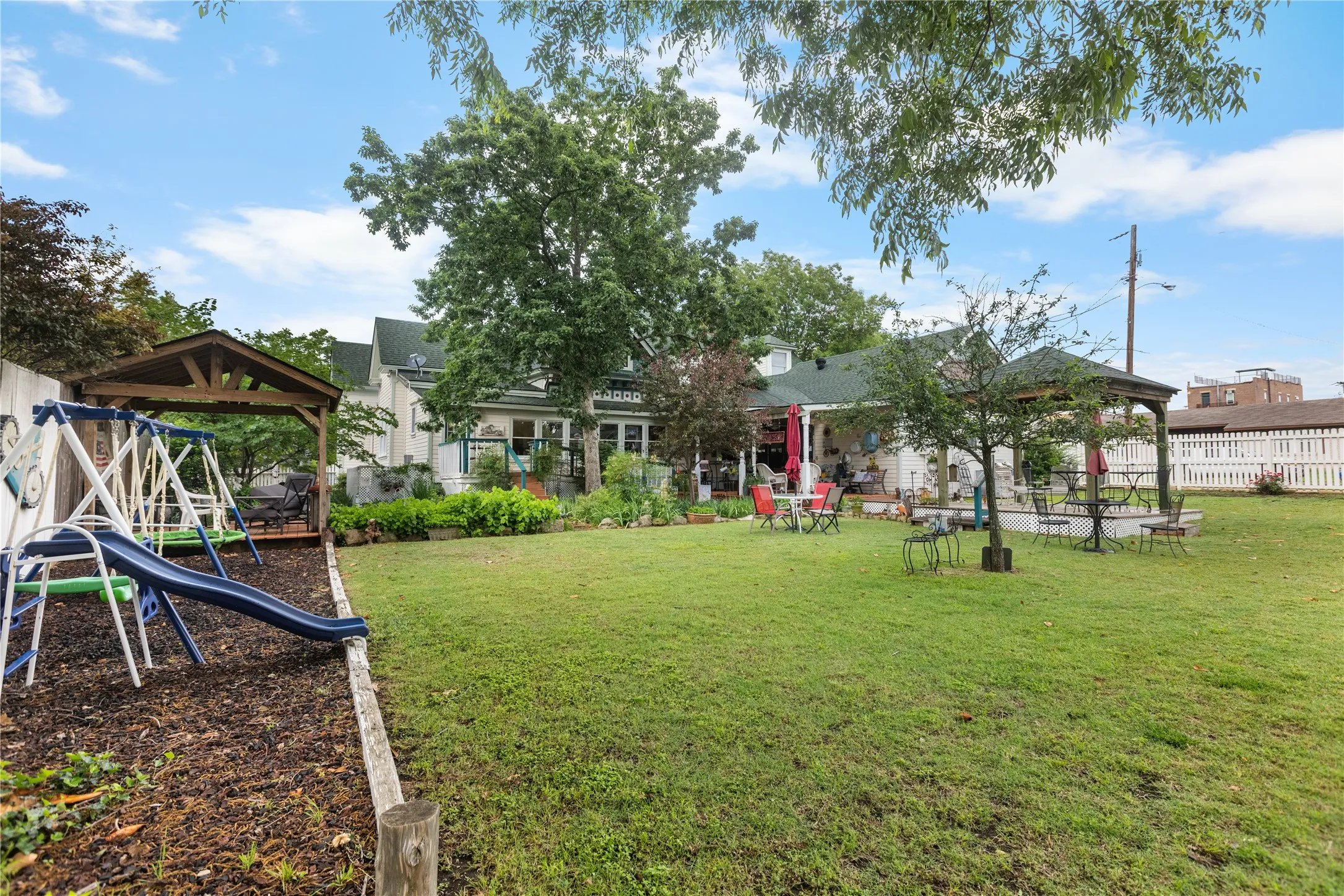 Expansive backyard featuring a large green lawn, a covered gazebo, and a dedicated play area with a wooden pergola