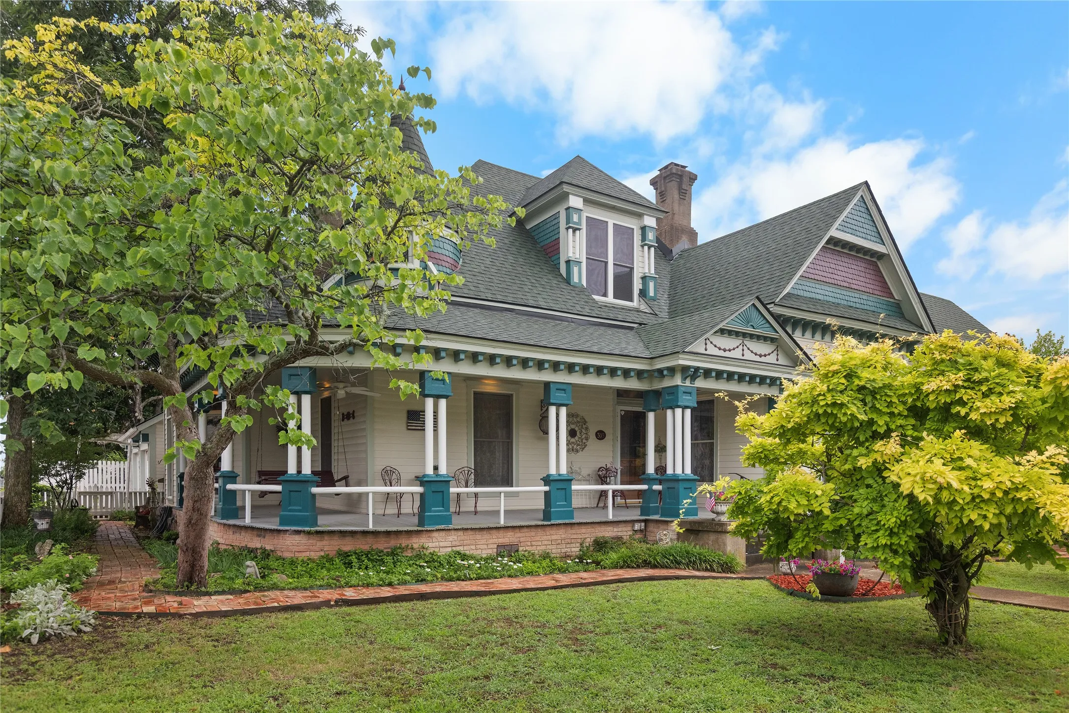 Victorian-style residence featuring a prominent wrap-around porch with decorative columns, a gabled roofline, and dormer windows