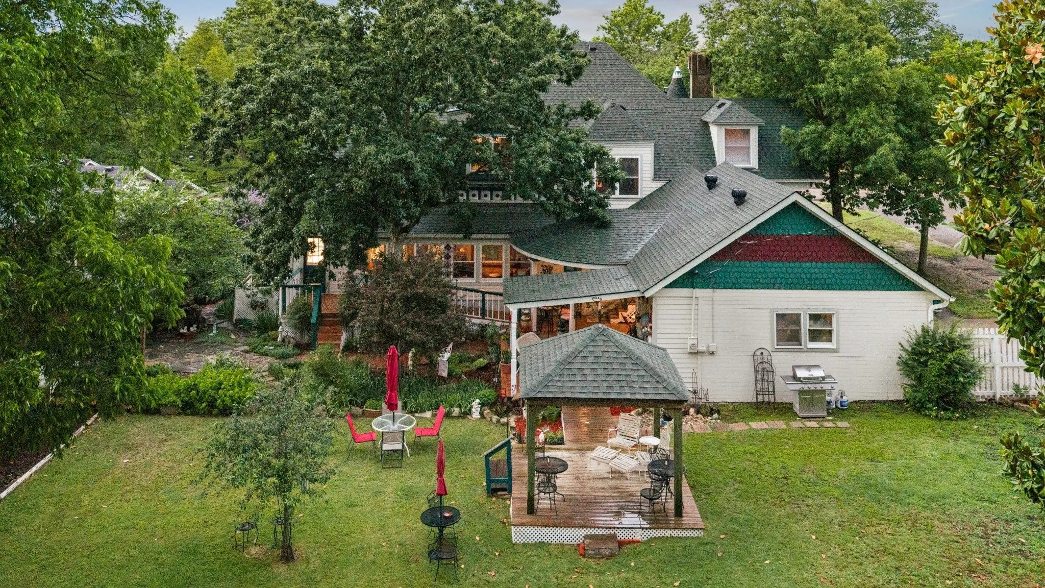 Expansive backyard featuring a gazebo with a shingled roof, a manicured lawn, mature trees, and a multi-level deck