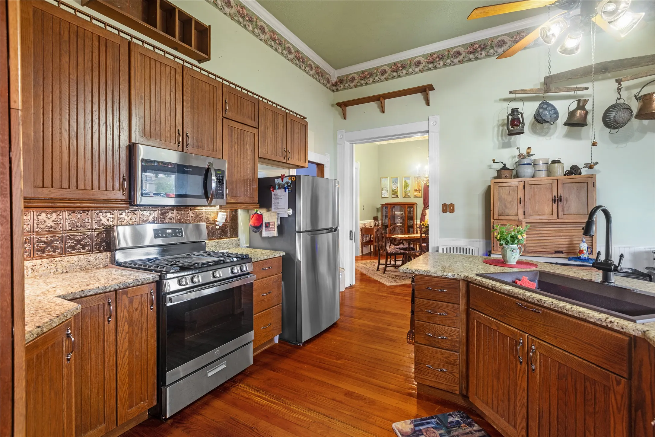 Kitchen featuring wood-finish cabinetry, granite-style countertops, stainless steel appliances, a tile backsplash, and wood-finish flooring