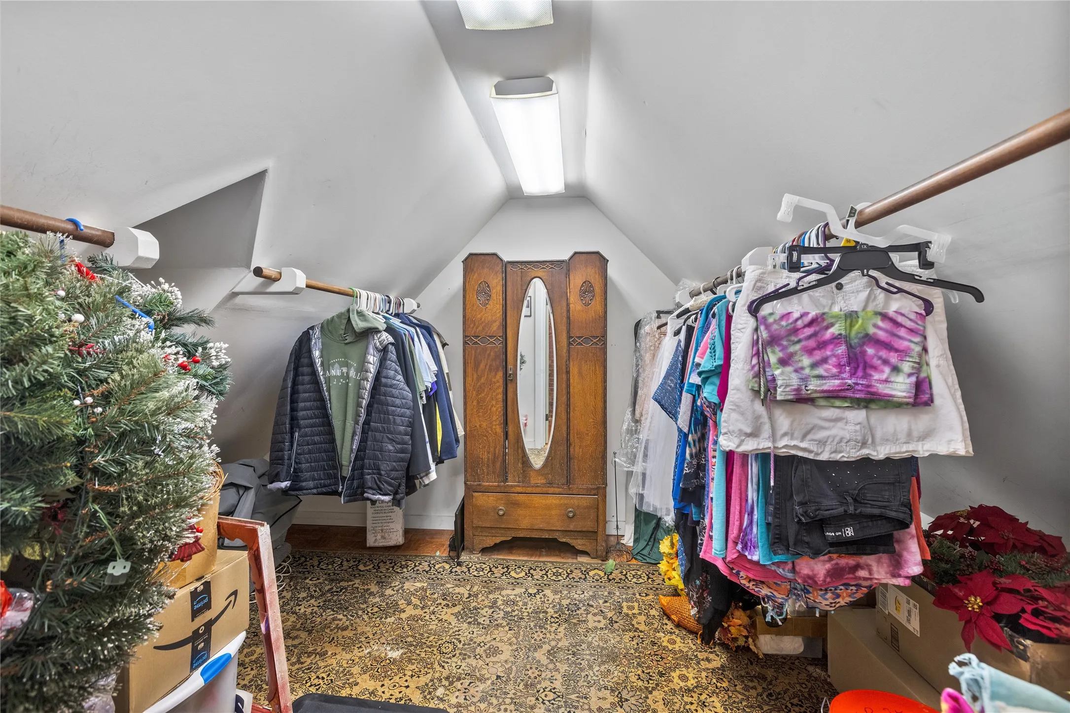 Sloped ceiling space featuring a vintage wooden armoire with an oval mirror, patterned carpet flooring, and integrated overhead lighting