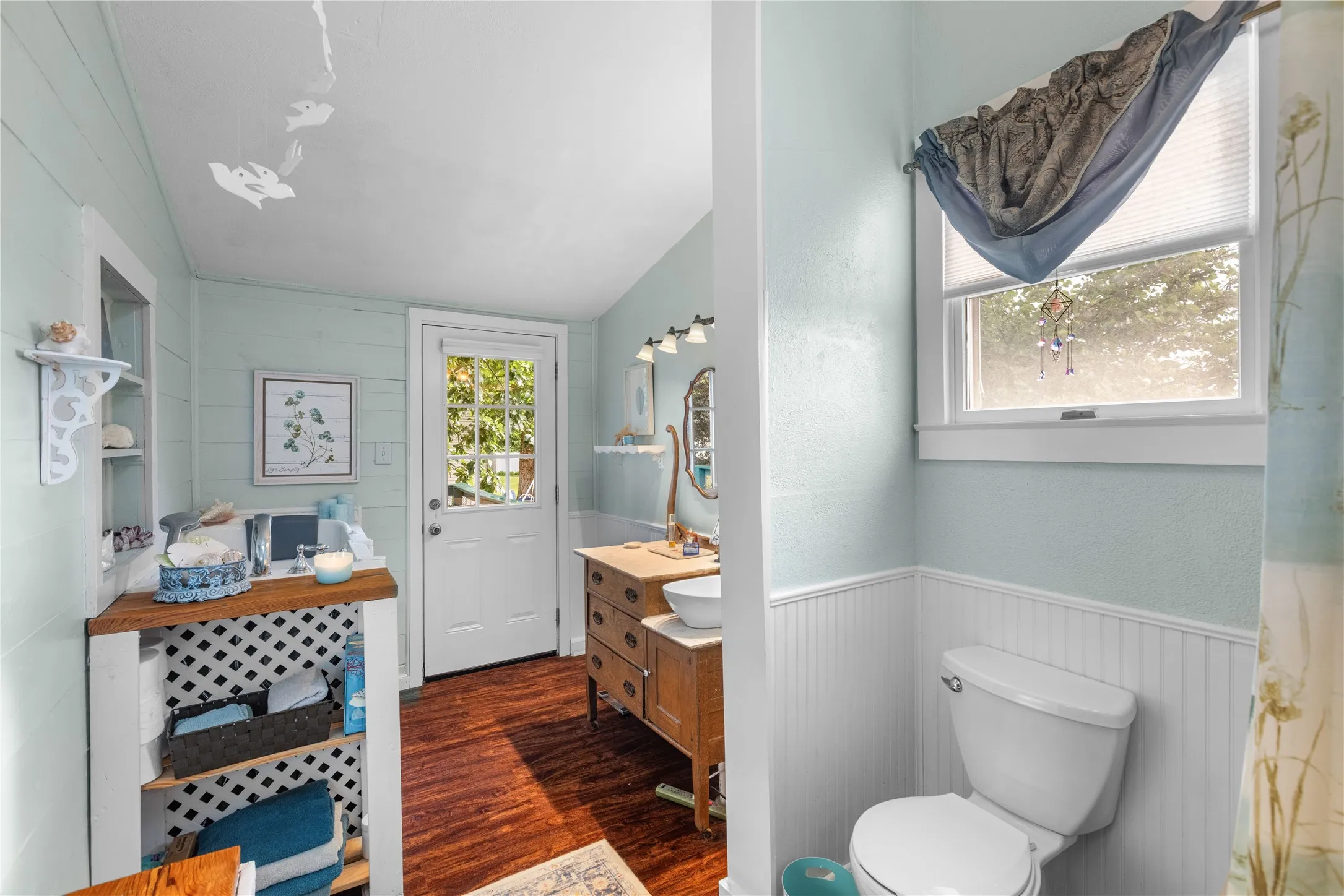 Downstairs primary Bathroom featuring wood-finish flooring, white shiplap walls, a white paneled door with glass inserts, and a vanity with a white vessel sink