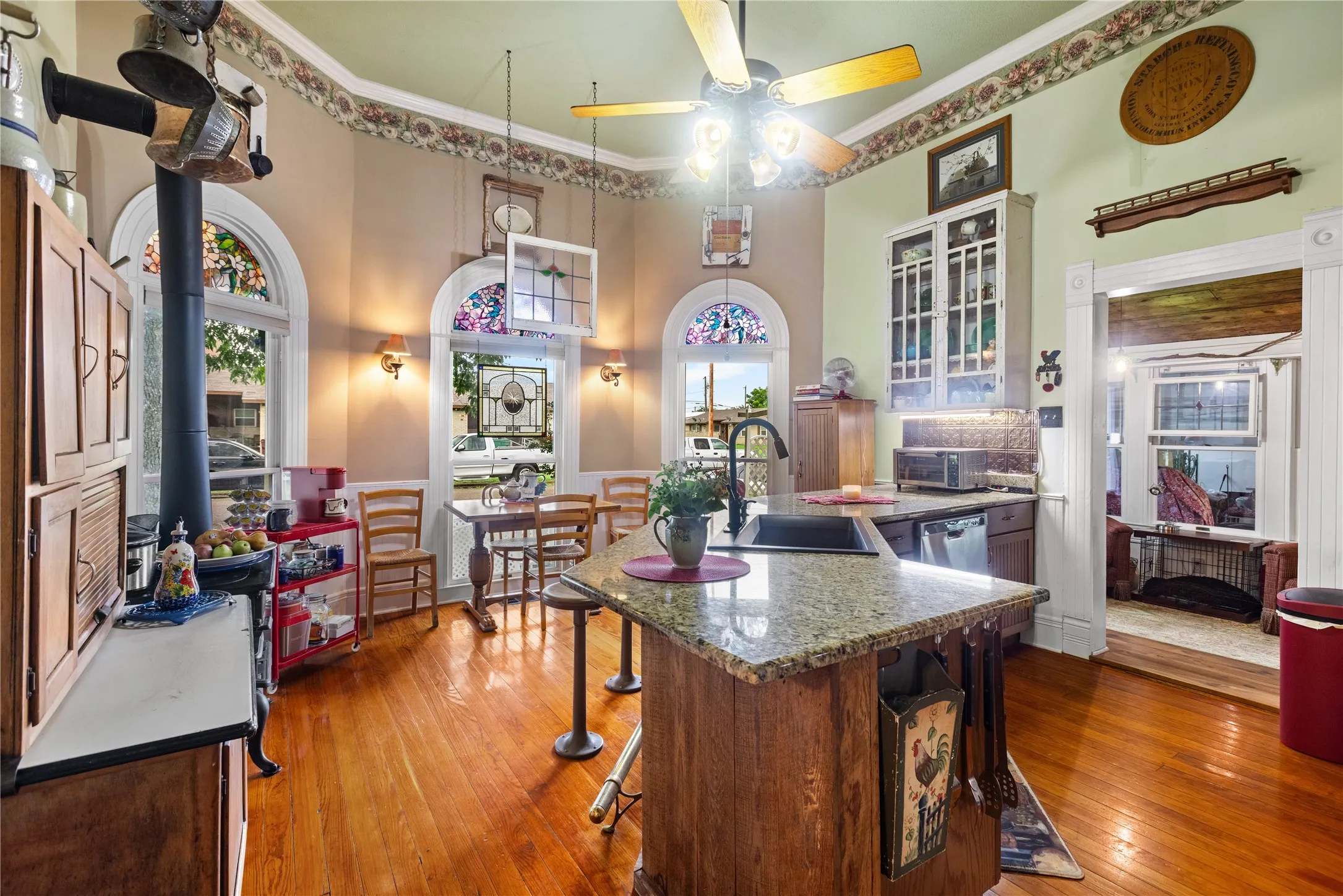 Kitchen featuring wood-finish flooring, an island with a countertop, arched windows with stained glass accents, and a built-in display cabinet with glass doors