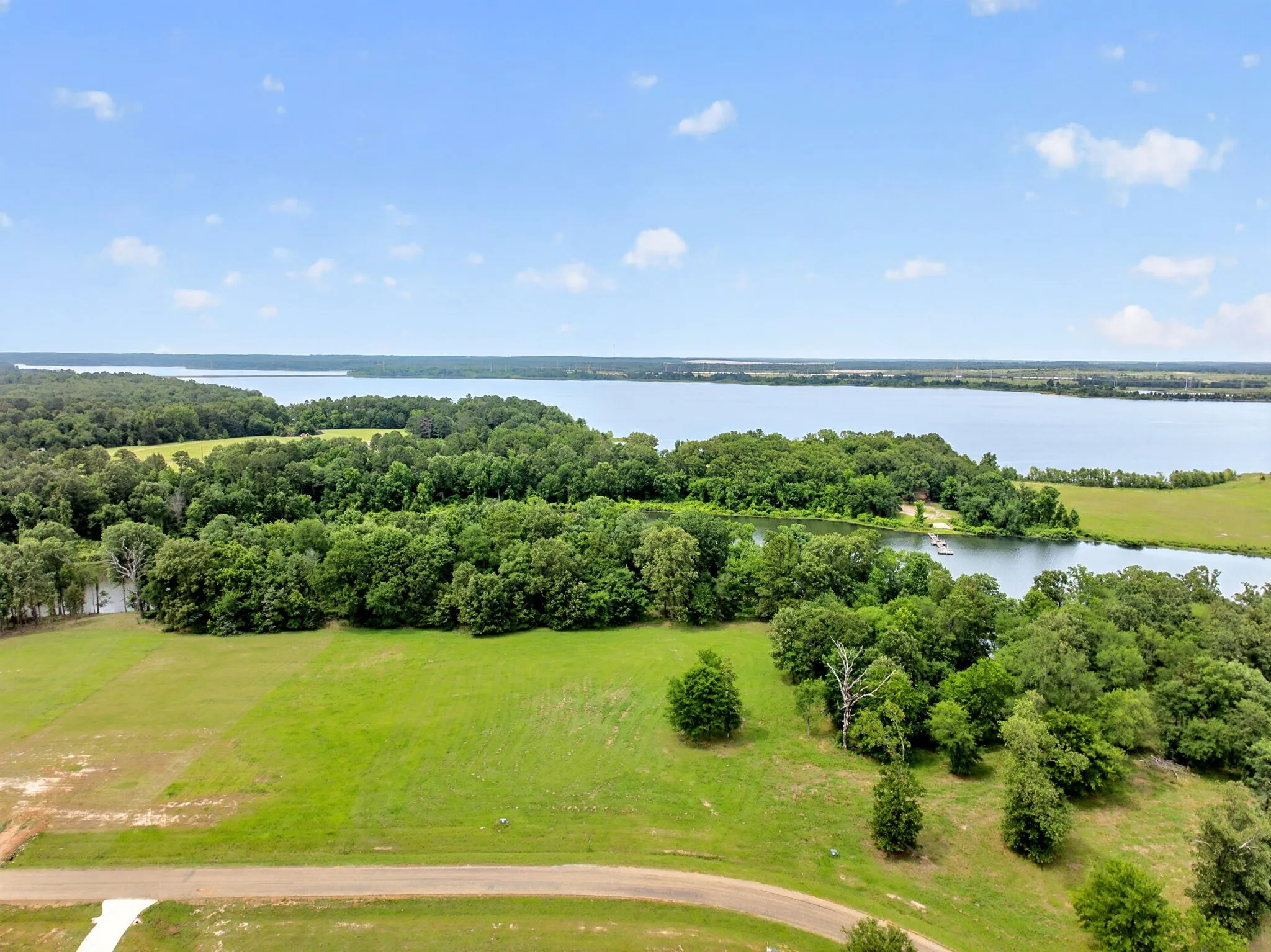 Expansive lakefront property featuring a private dock, lush green fields, and mature tree lines
