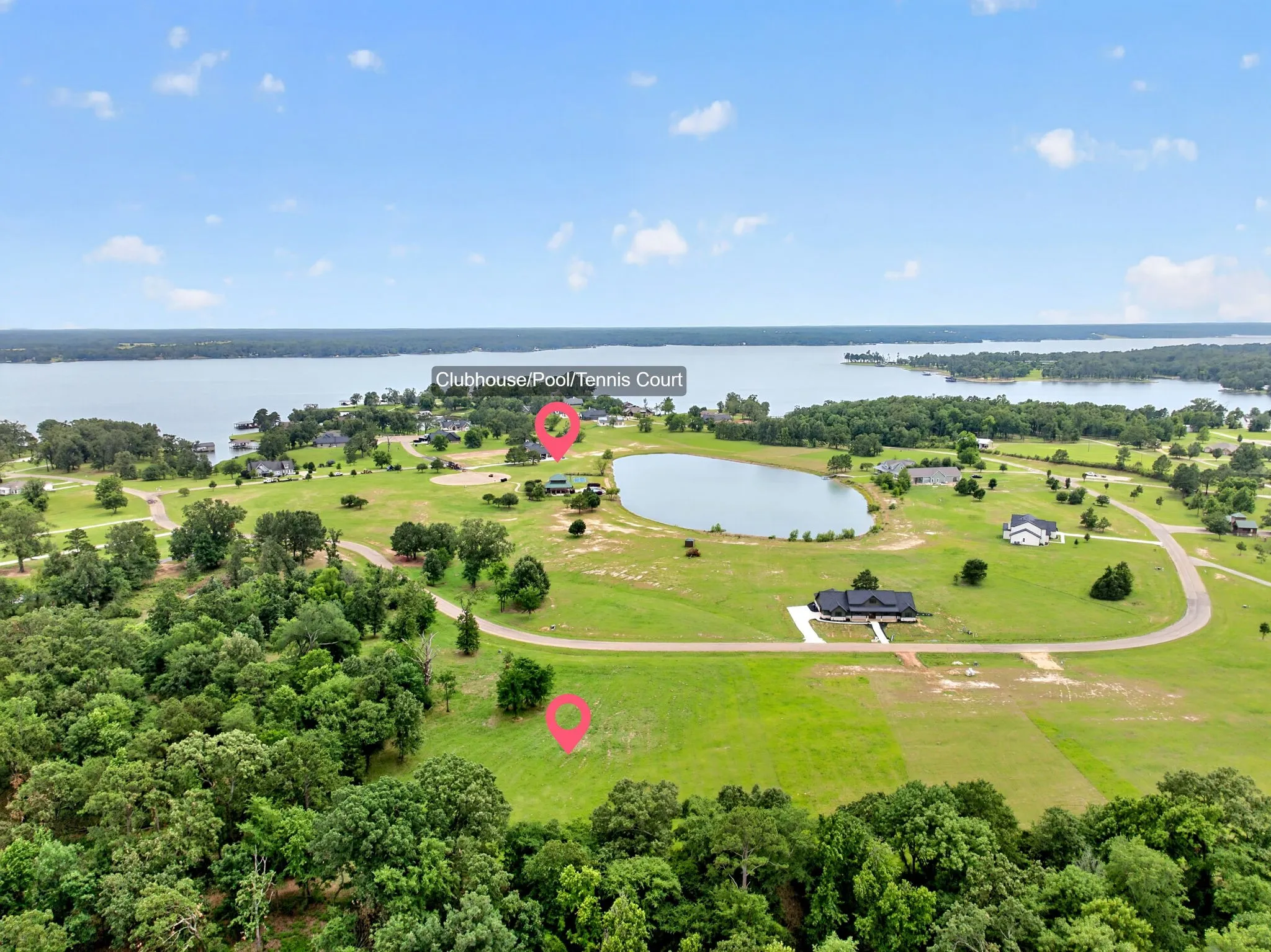 Expansive aerial captures a large body of water, a smaller pond, and residential structures amidst green landscapes