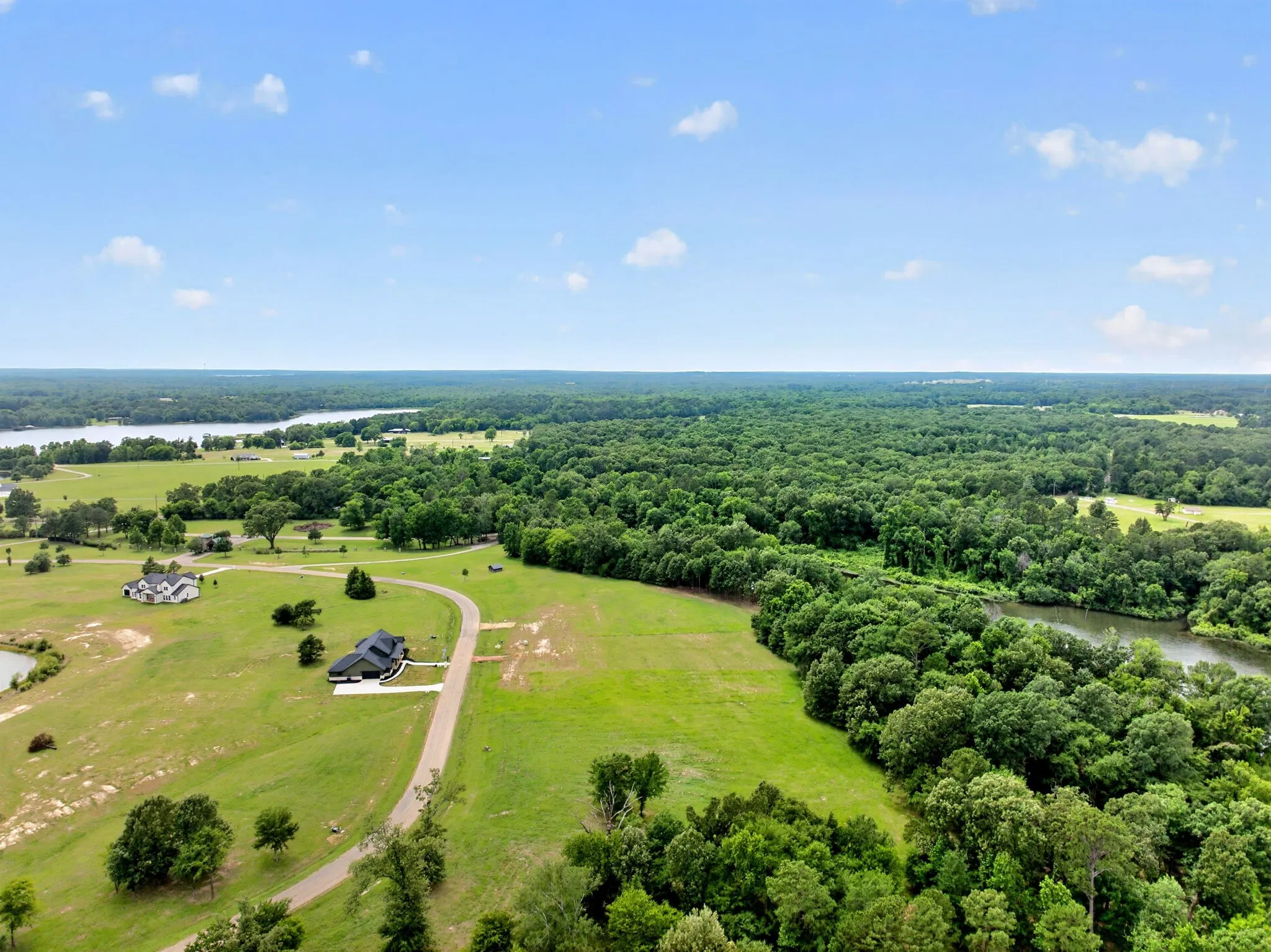 Expansive property featuring a contemporary residence, a winding driveway, and a large body of water in the background