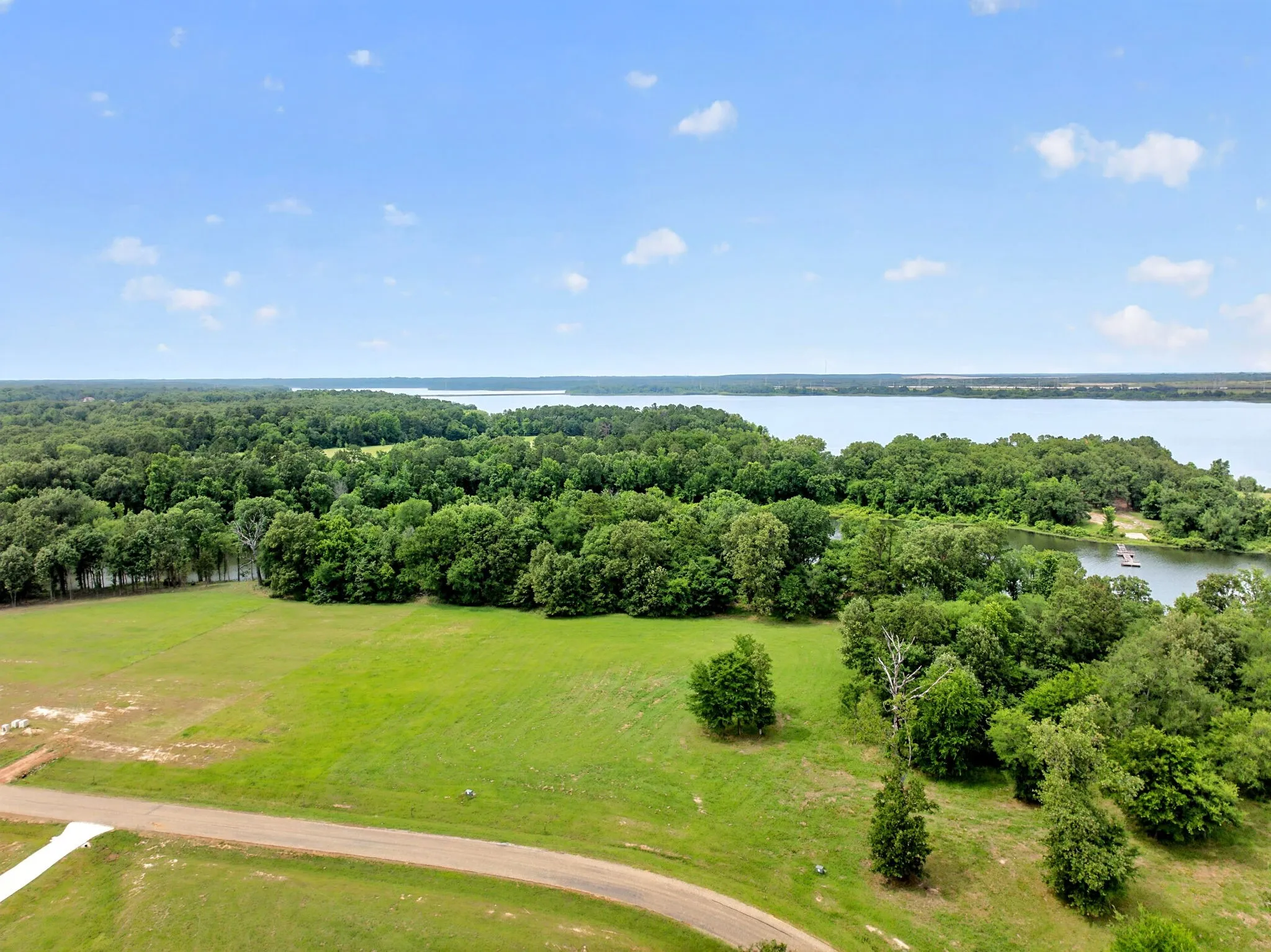 Expansive lot featuring a green lawn, mature trees, and a paved road