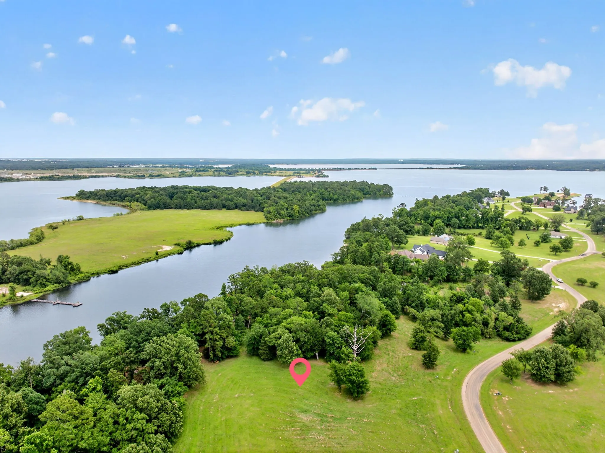 Expansive waterfront land parcel featuring mature trees, a gentle slope, and direct access to a paved road