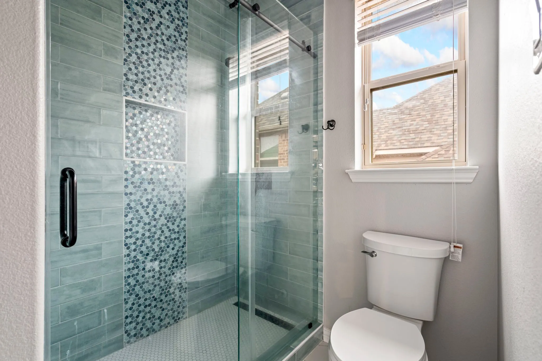 The gorgeous upstairs bathroom serving the secondary bedrooms features a stunning new tile shower surround with sleek glass sliding doors, creating a fresh, modern, and beautifully updated space.