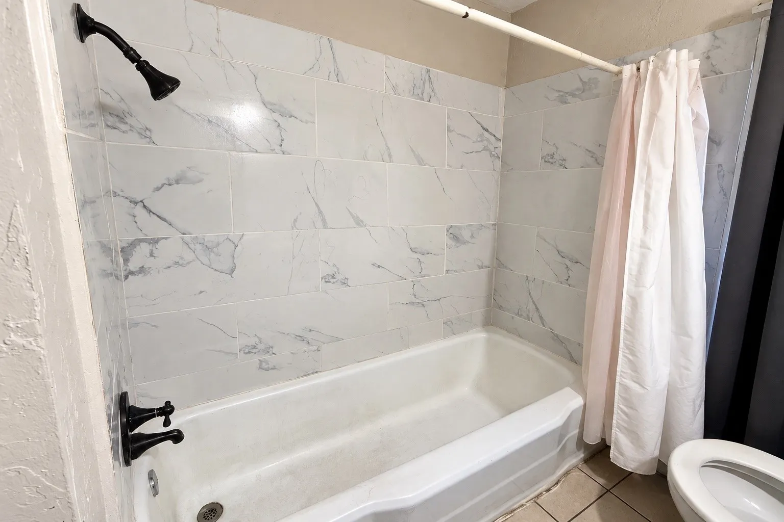 Bathtub with a white finish, subway-style wall tiling featuring a grey and white marble-look pattern, and matte black plumbing fixtures