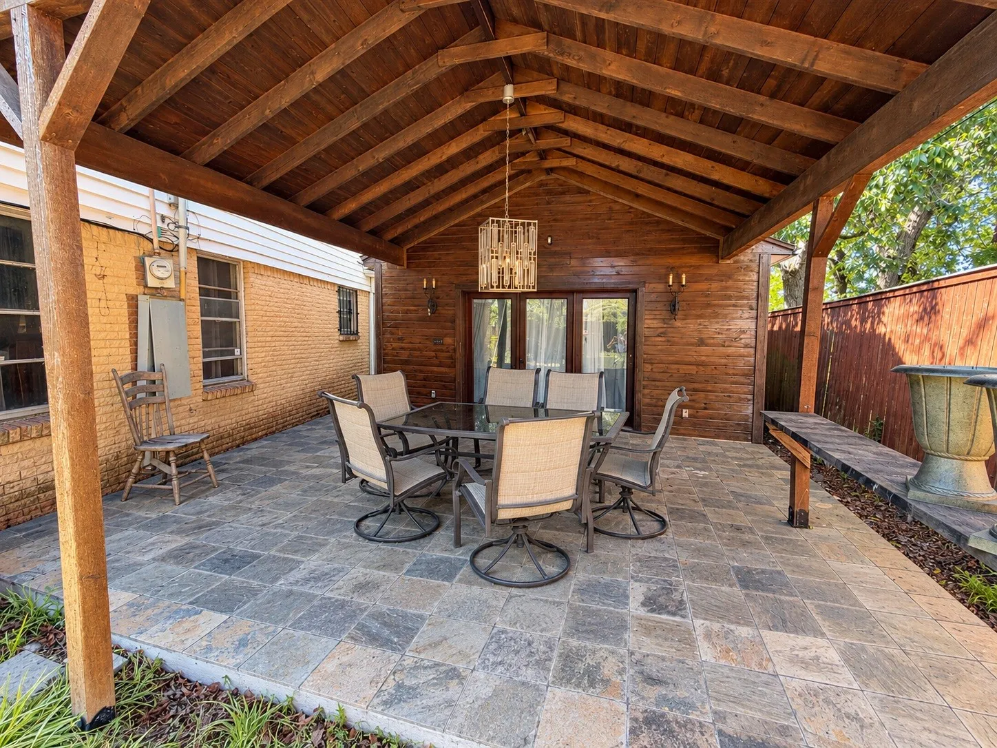 Covered outdoor patio with a wood-finish ceiling, stone paver flooring, and integrated lighting fixtures