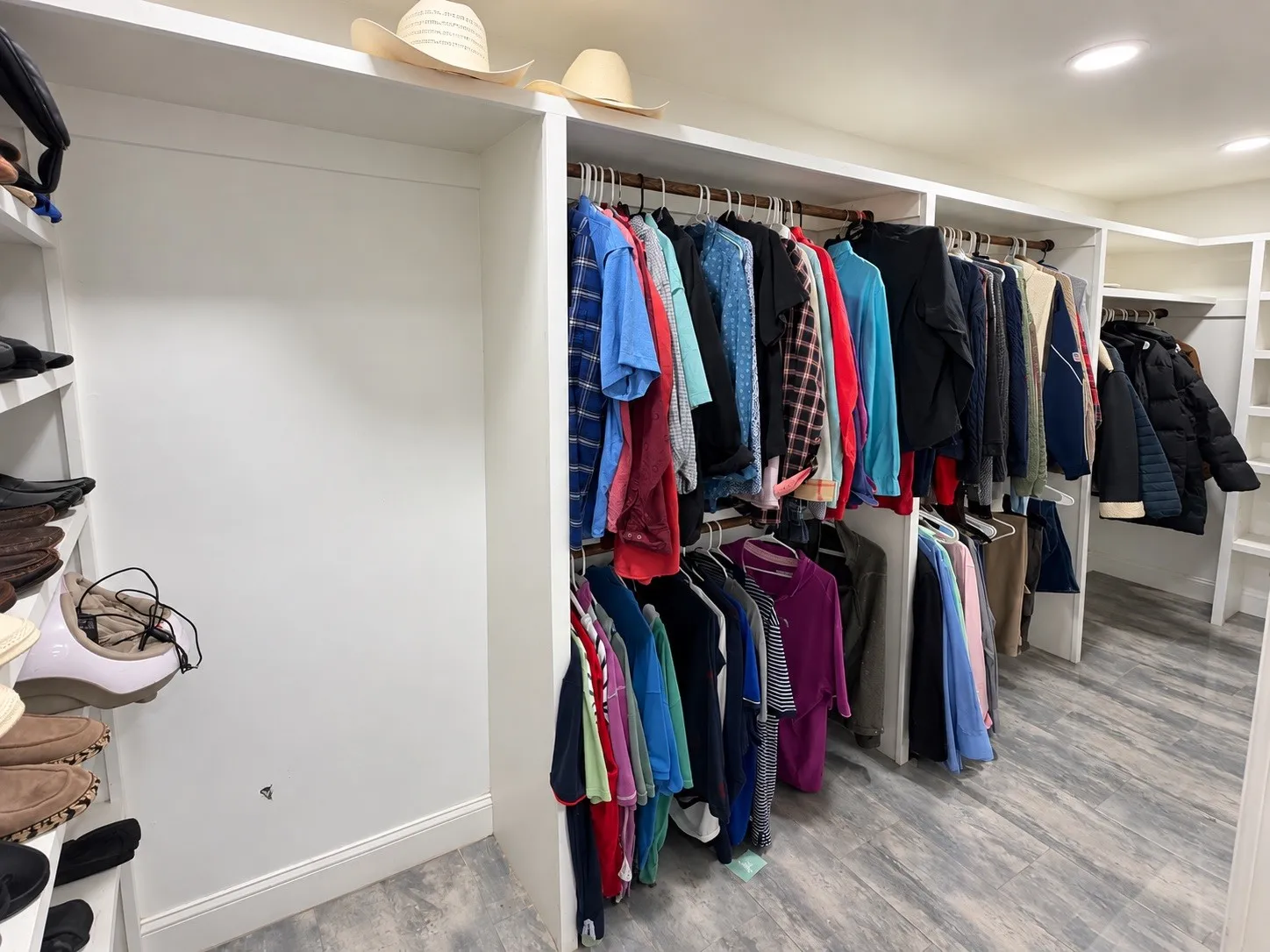 Built-in closet system with multiple hanging rods, recessed lighting, and wood-finish flooring