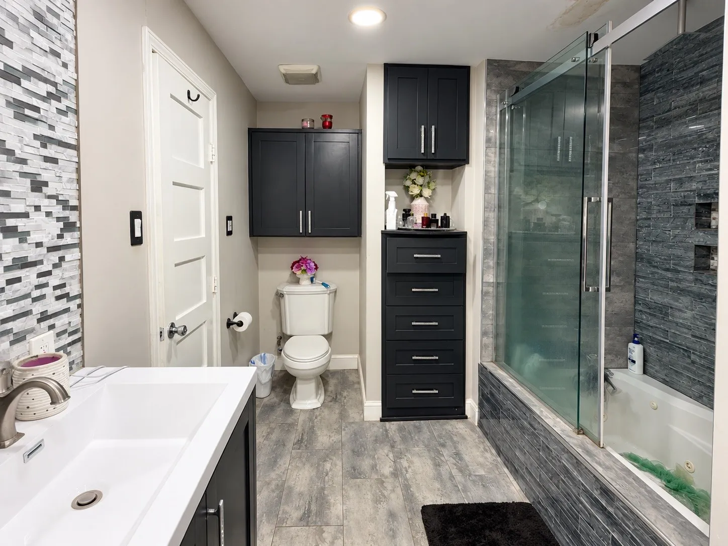 Full bathroom featuring a rectangular integrated sink, wood-finish flooring, built-in cabinetry, and a shower with a sliding glass door and tiled surround