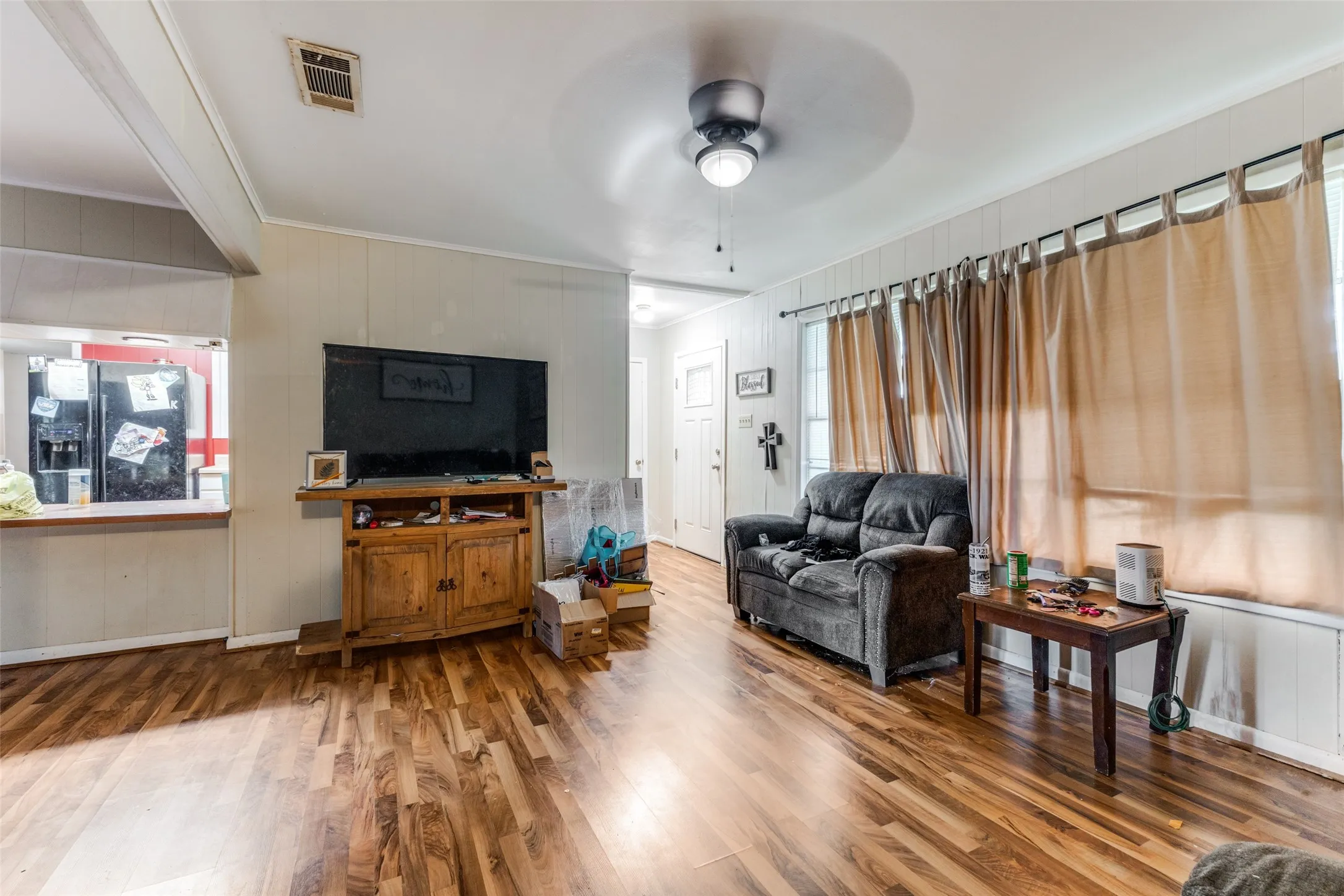 Living room featuring ornamental molding, wood finished floors, wood walls, and a ceiling fan
