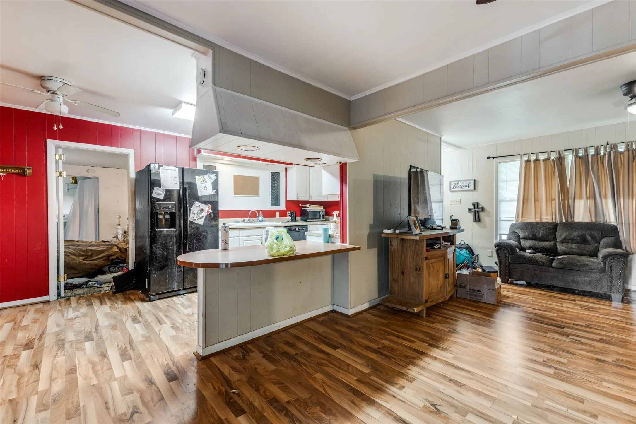 Kitchen with a ceiling fan, open floor plan, black fridge, light wood-style floors, and wooden walls