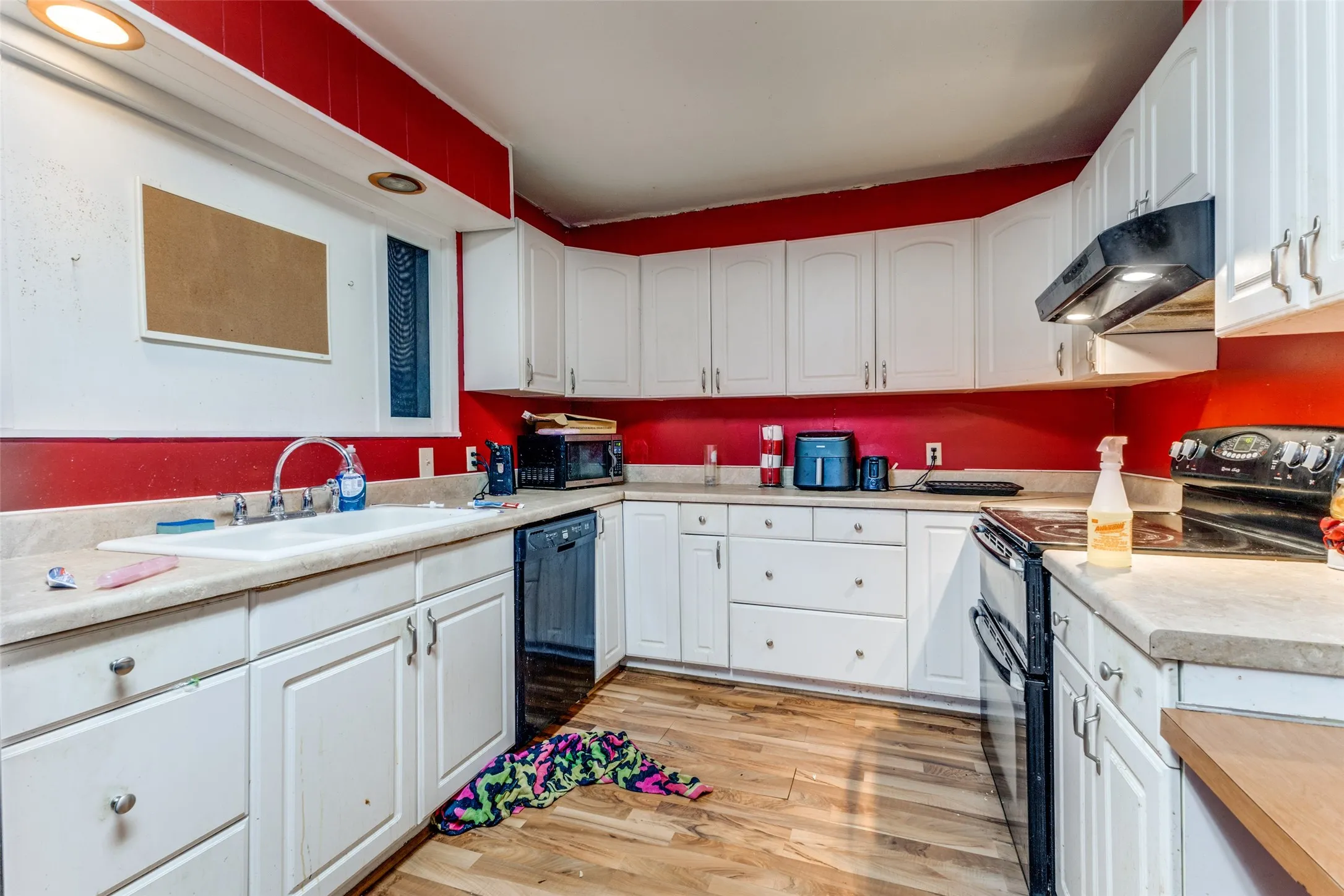 Kitchen with black appliances, white cabinets, light countertops, under cabinet range hood, and light wood finished floors
