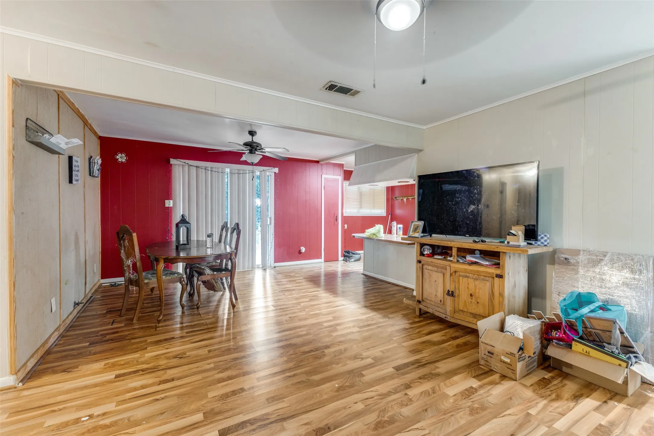 Living room featuring light wood-style floors, wood walls, crown molding, and a ceiling fan