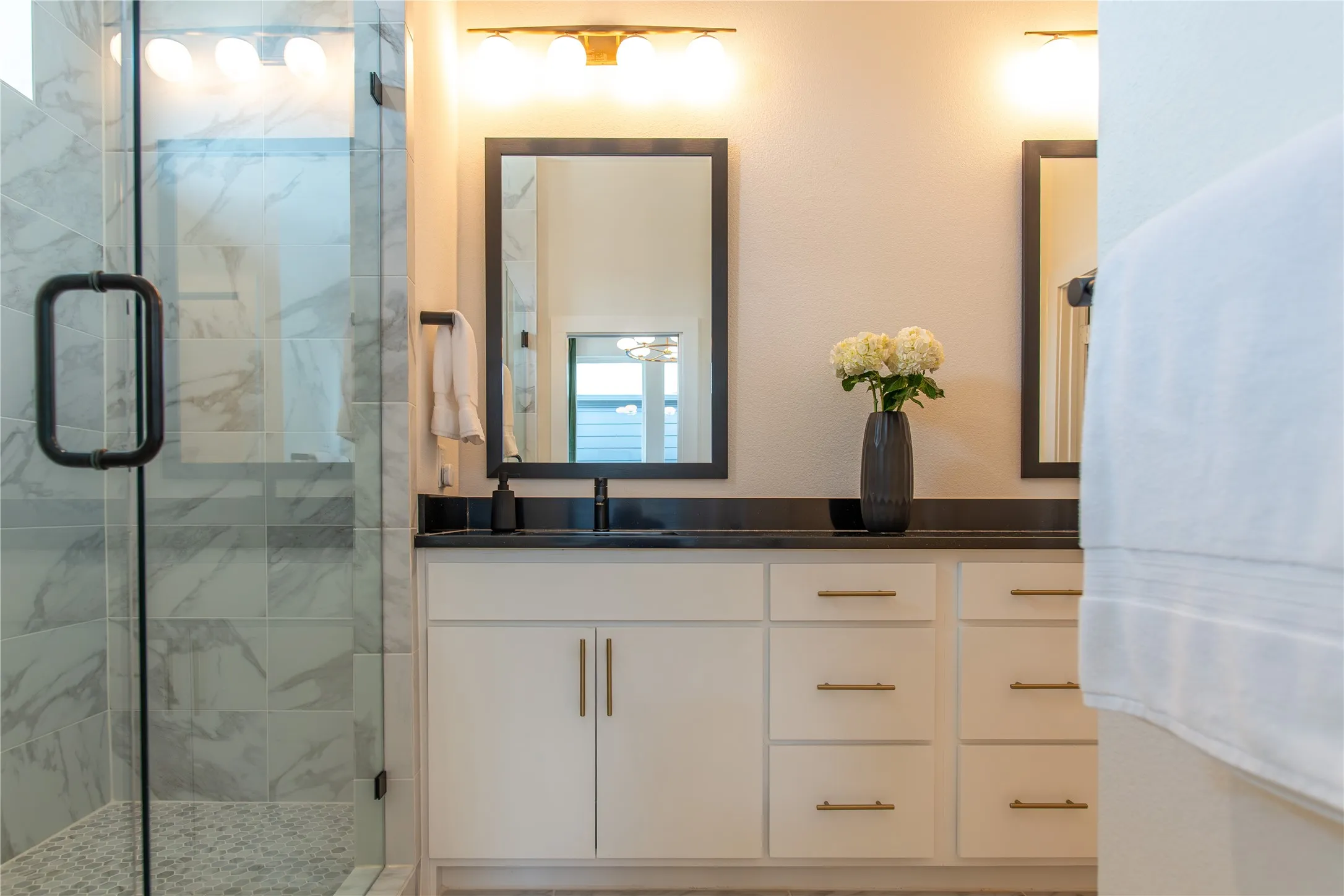 Bathroom featuring a dual vanity, dark stone countertop, and two framed mirrors with individual lighting fixtures