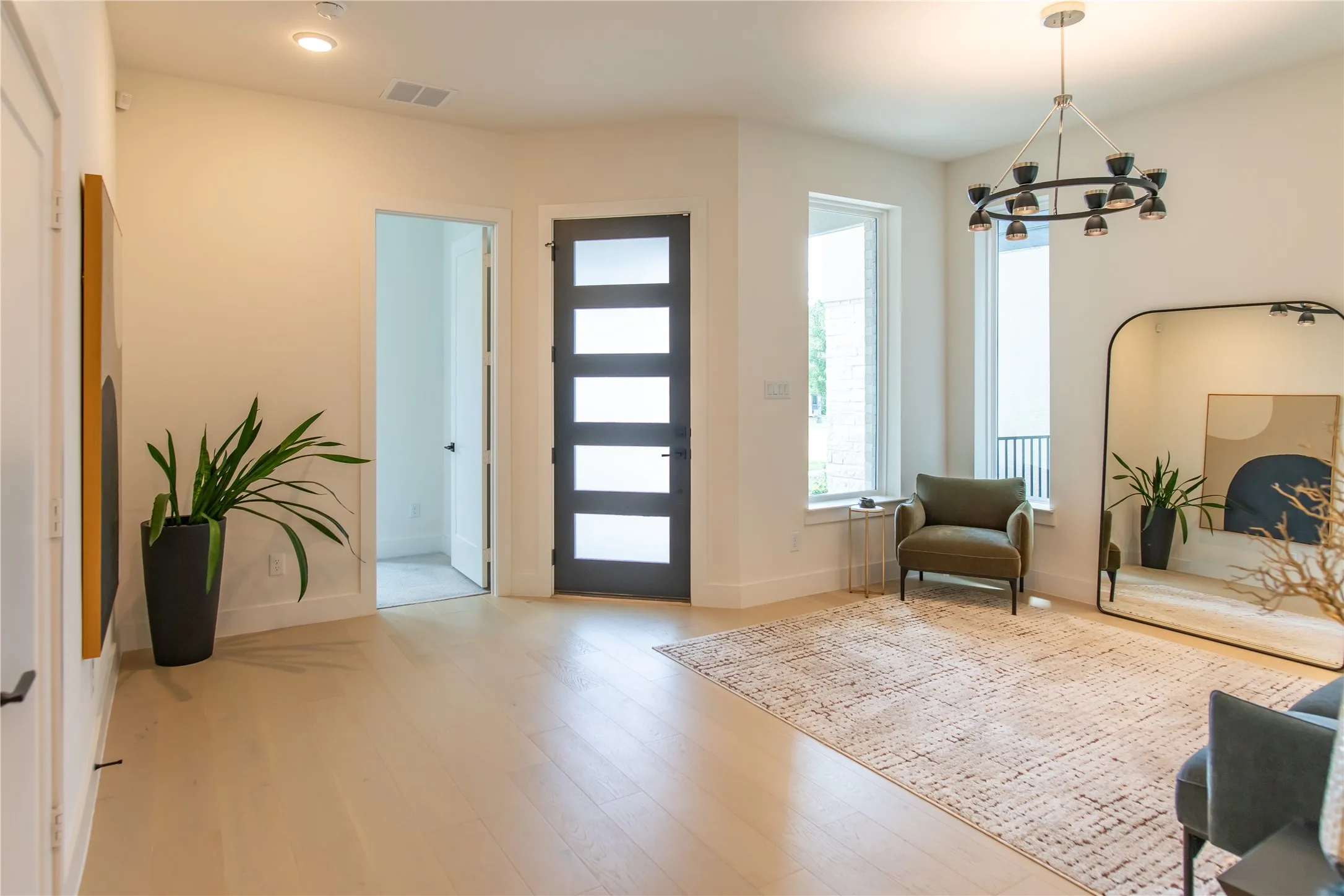 Spacious entry foyer featuring light wood-finish flooring, a contemporary front door with frosted glass panels, recessed ceiling lighting, and a modern chandelier