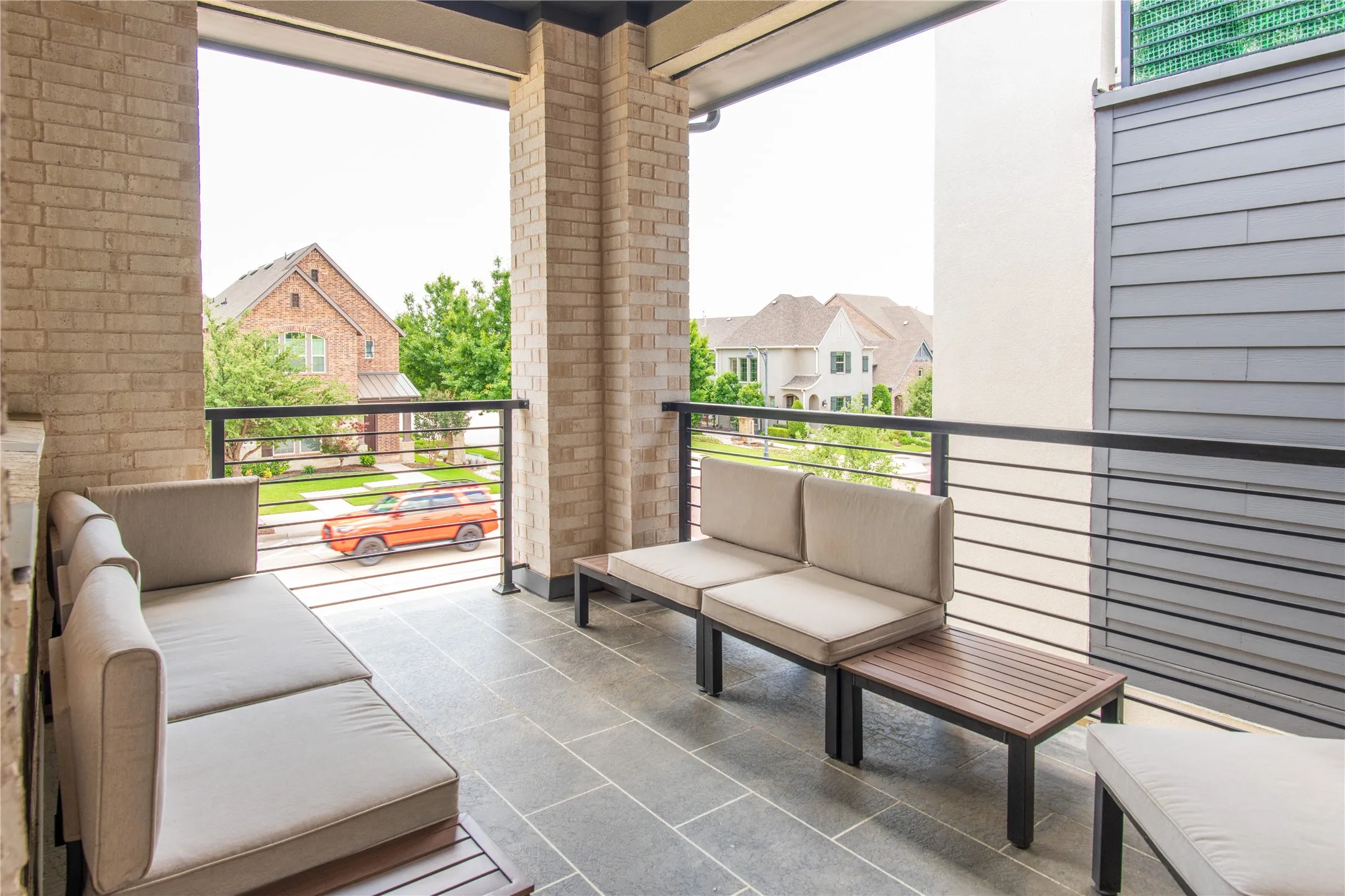 Covered outdoor balcony featuring stone tile flooring, brick columns, and horizontal bar railing