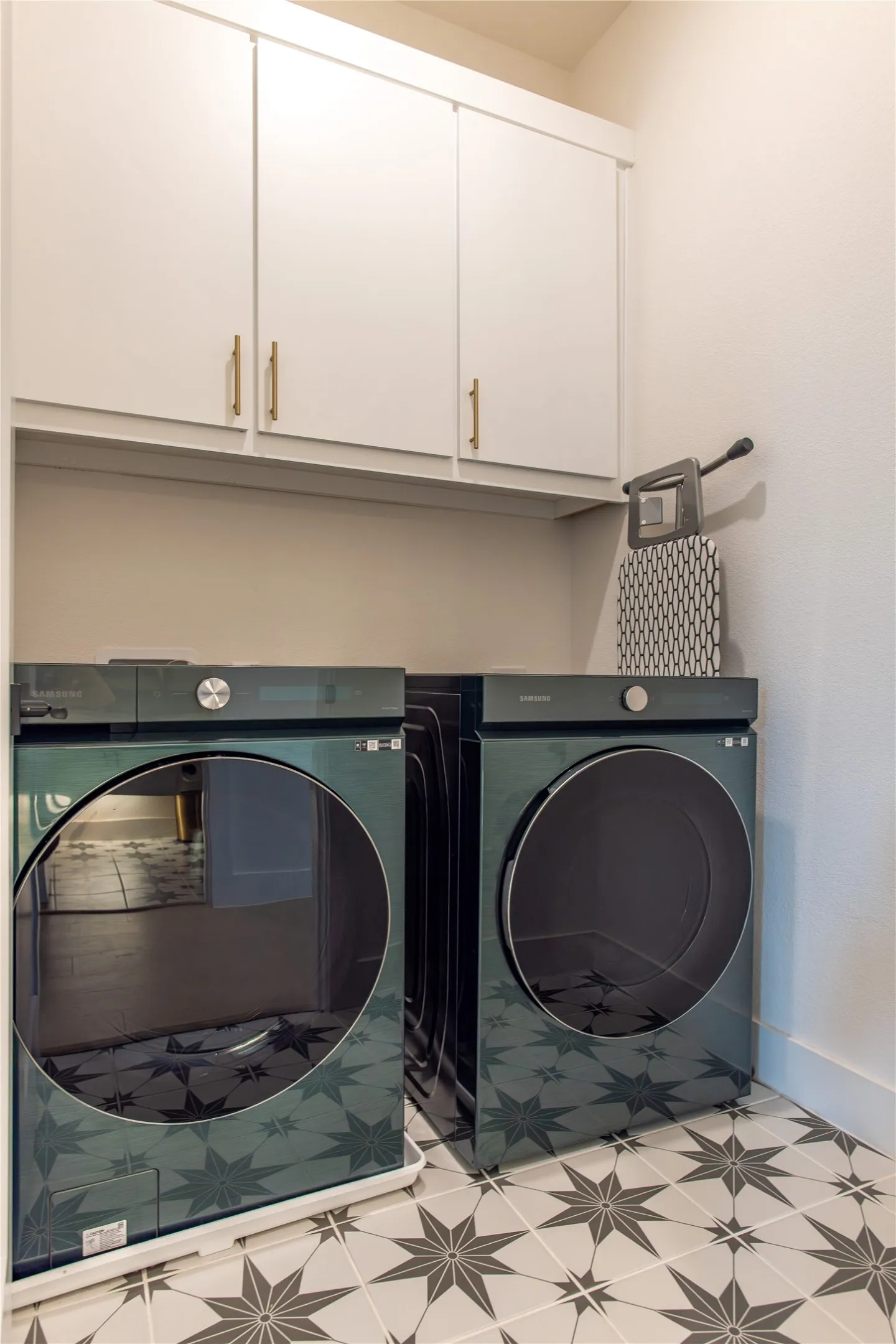 Laundry area featuring patterned floor tile, white shaker-style cabinetry with gold-tone hardware, and painted walls