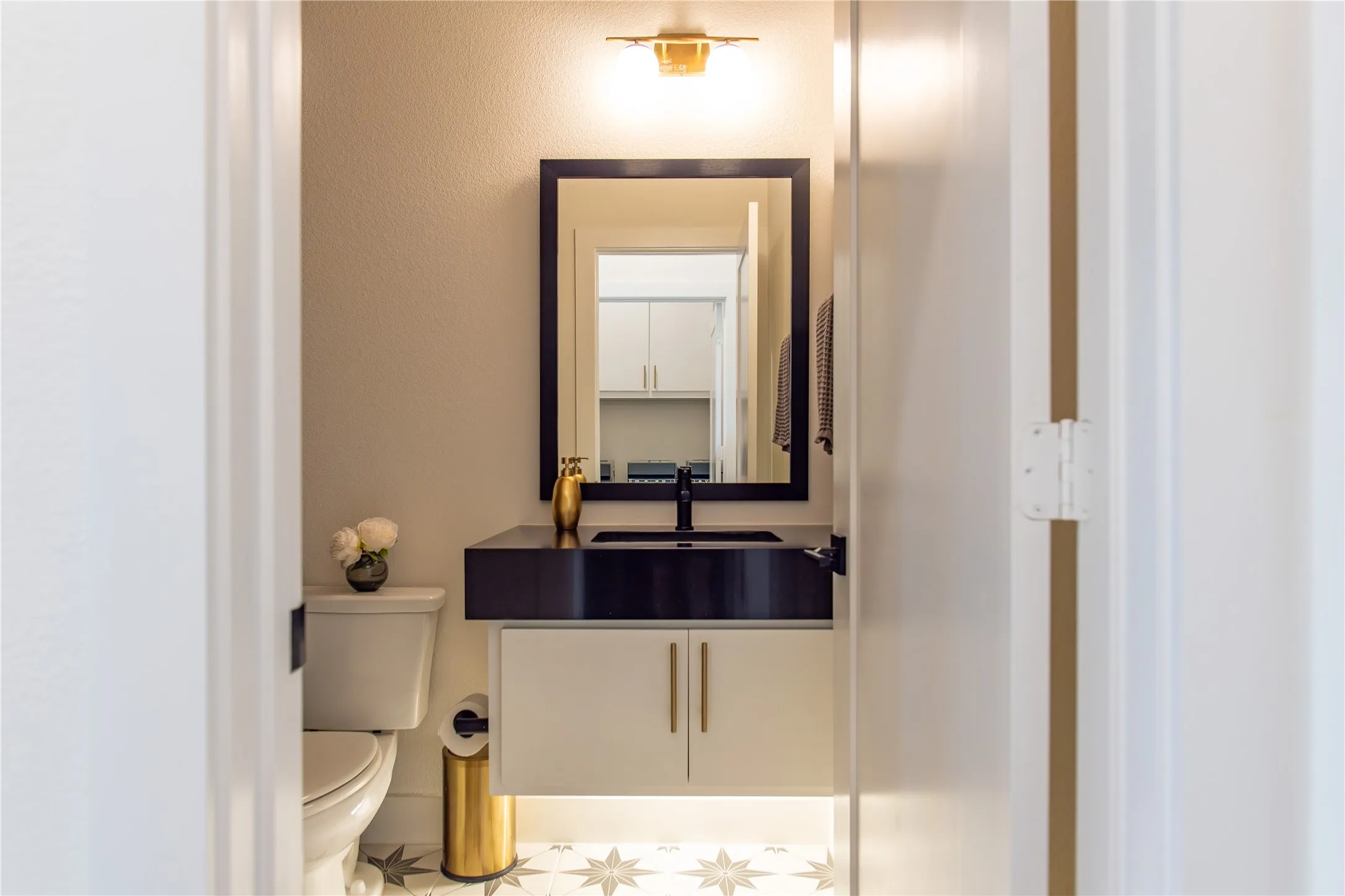 Powder room featuring a floating vanity with a matte black countertop and integrated sink, a rectangular mirror, and a gold-tone wall sconce