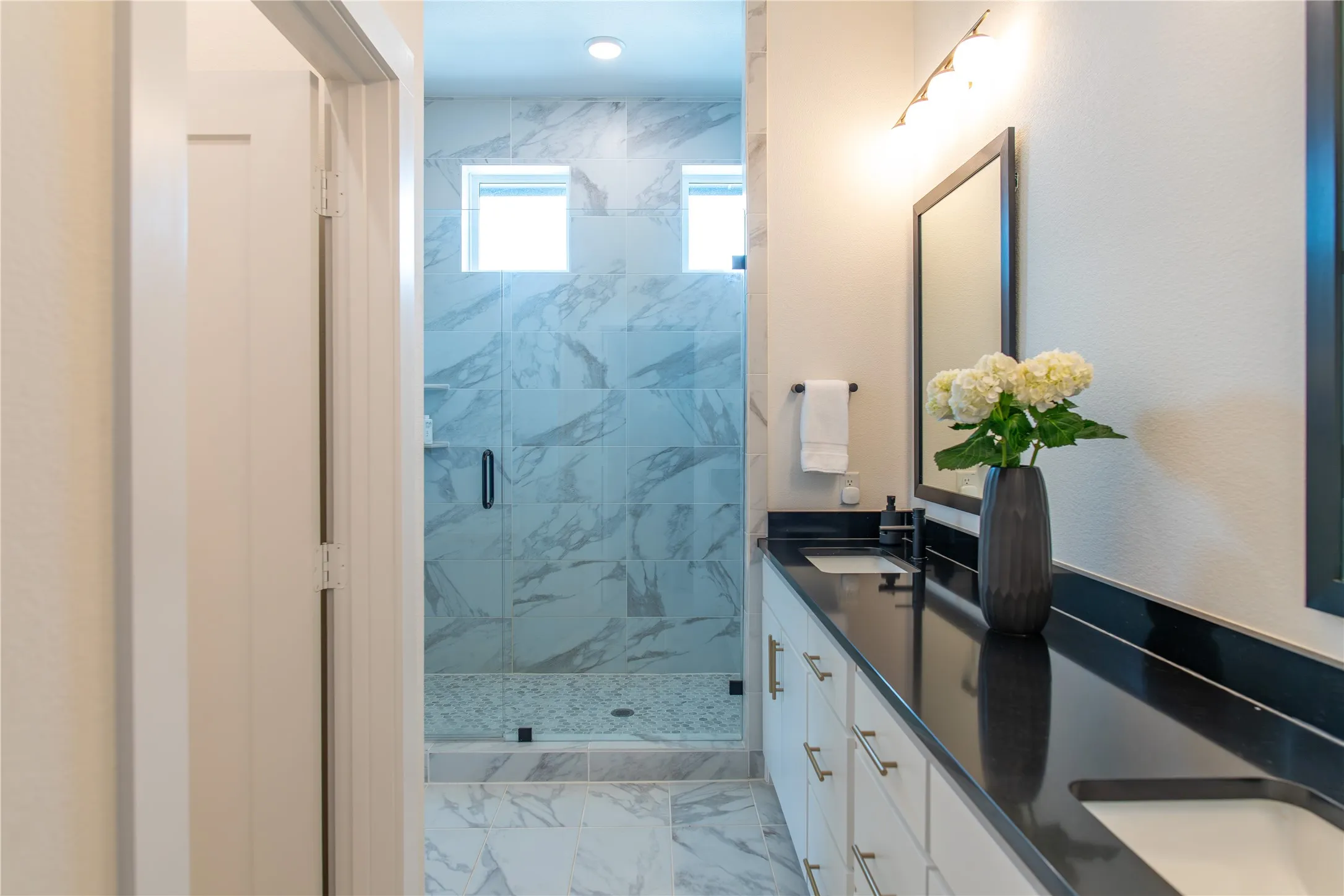 Contemporary bathroom featuring dual vanity with black countertops, white cabinetry, and undermount sinks