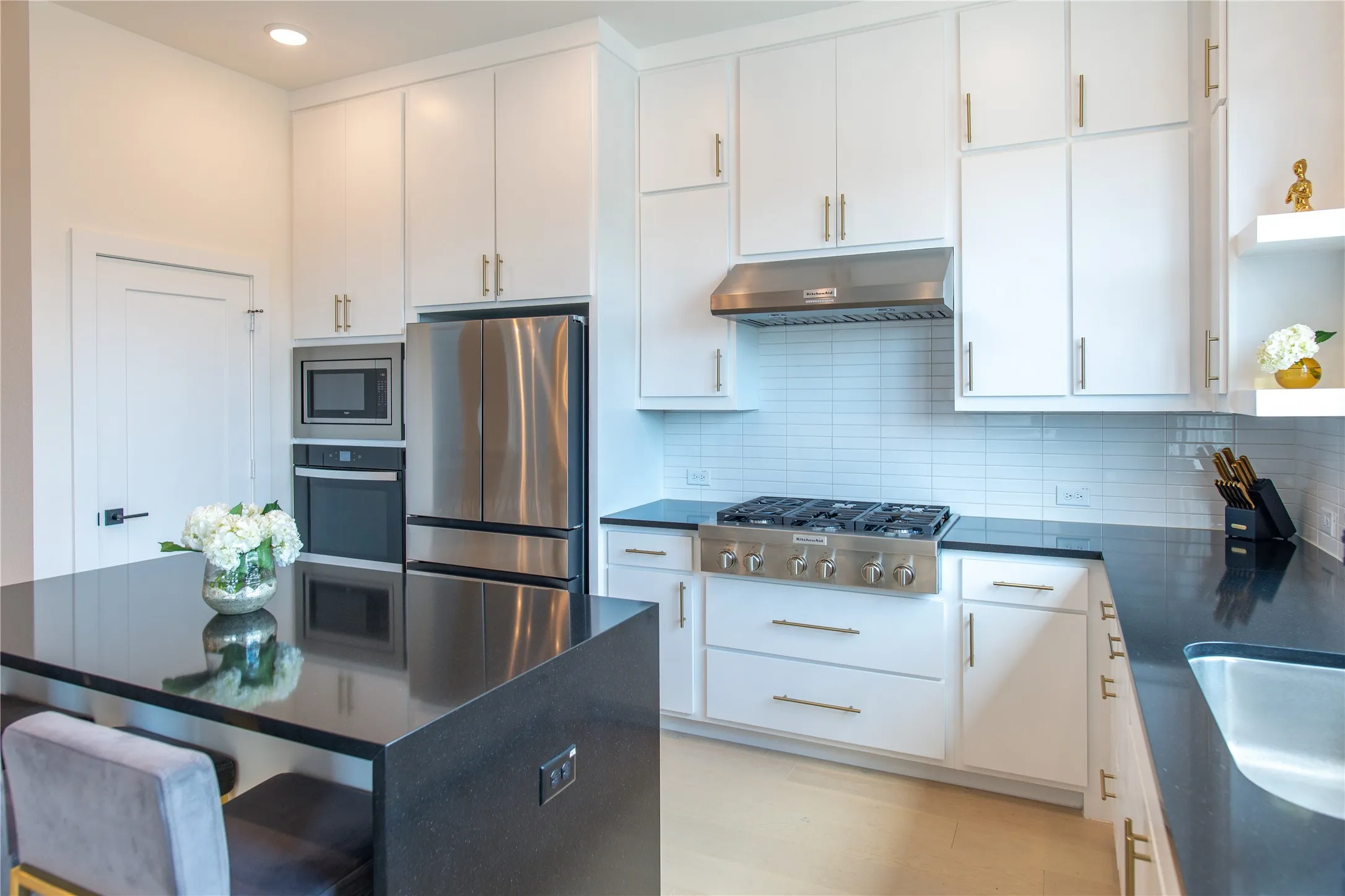 Modern kitchen featuring white cabinetry, dark countertops, a stainless steel gas range with hood, a built-in oven, and light wood-finish flooring