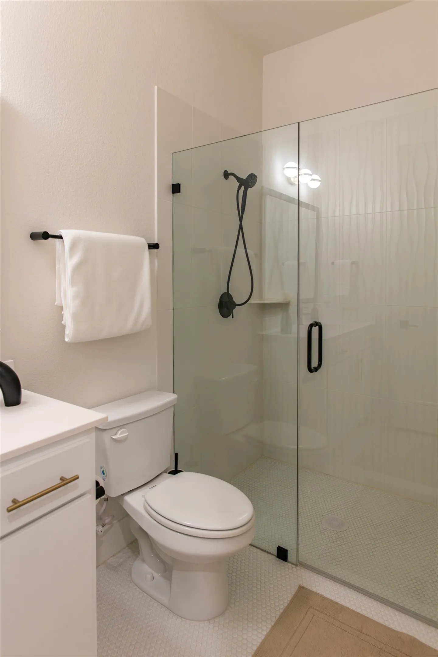 Walk-in shower featuring a glass enclosure, matte black fixtures, and a white textured tile surround