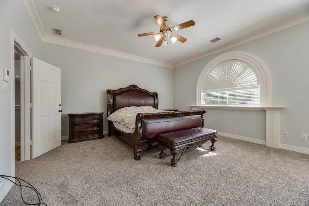 Spacious room featuring a prominent arched window with louvered blinds, crown molding, and neutral-toned carpeting