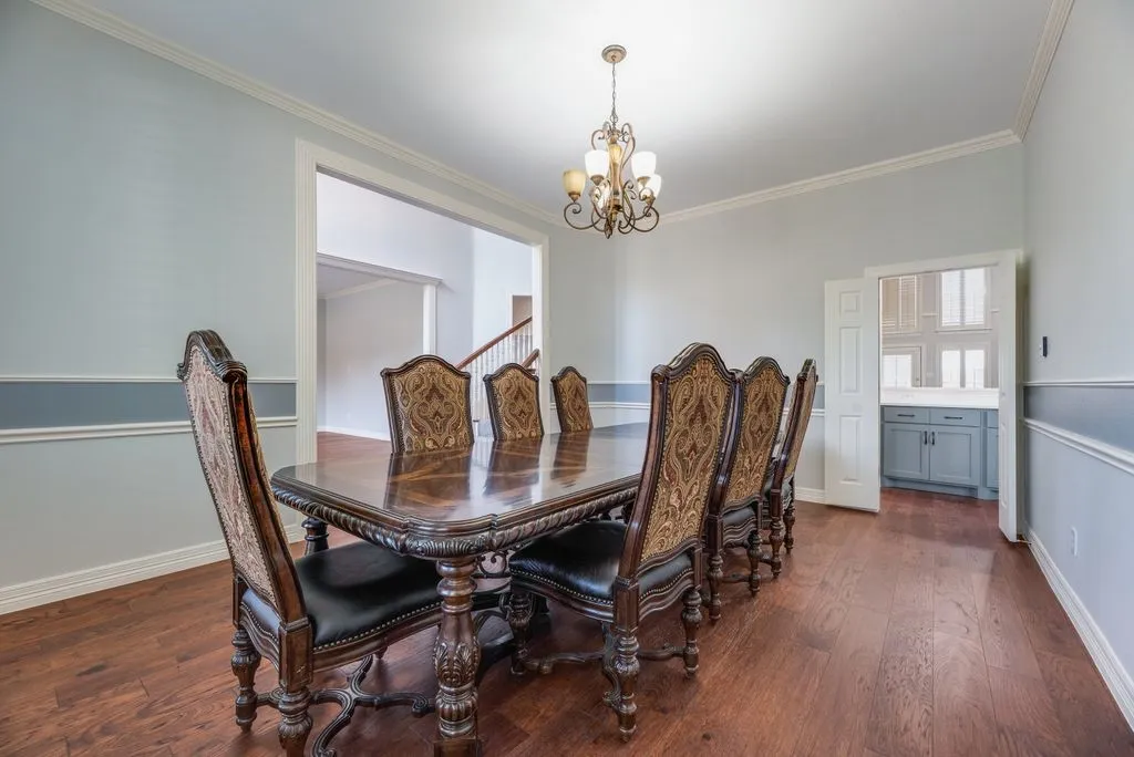 Formal dining room featuring wood-finish flooring, two-tone wall treatment with wainscoting, a detailed chandelier, and crown molding