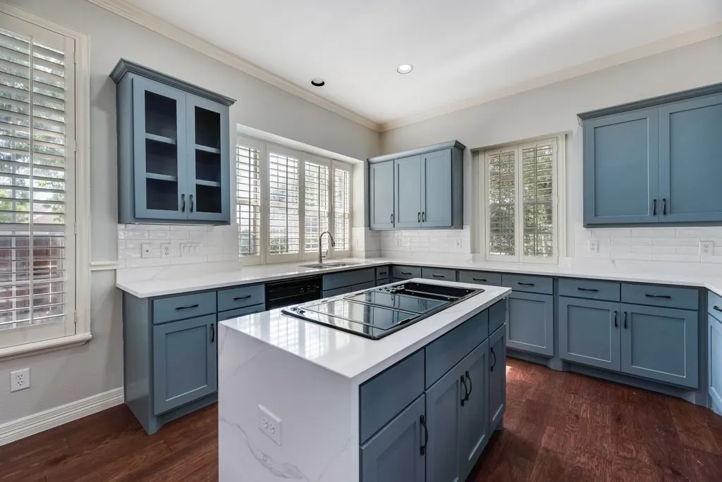 Spacious kitchen featuring custom blue cabinetry, white quartz countertops, subway tile backsplash, a center island with integrated cooktop, and wood-finish flooring