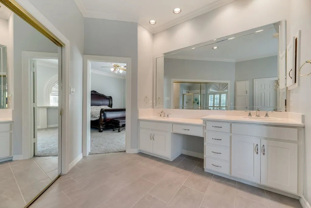 Spacious bathroom featuring dual vanities with white cabinetry, a large integrated mirror, and tile flooring