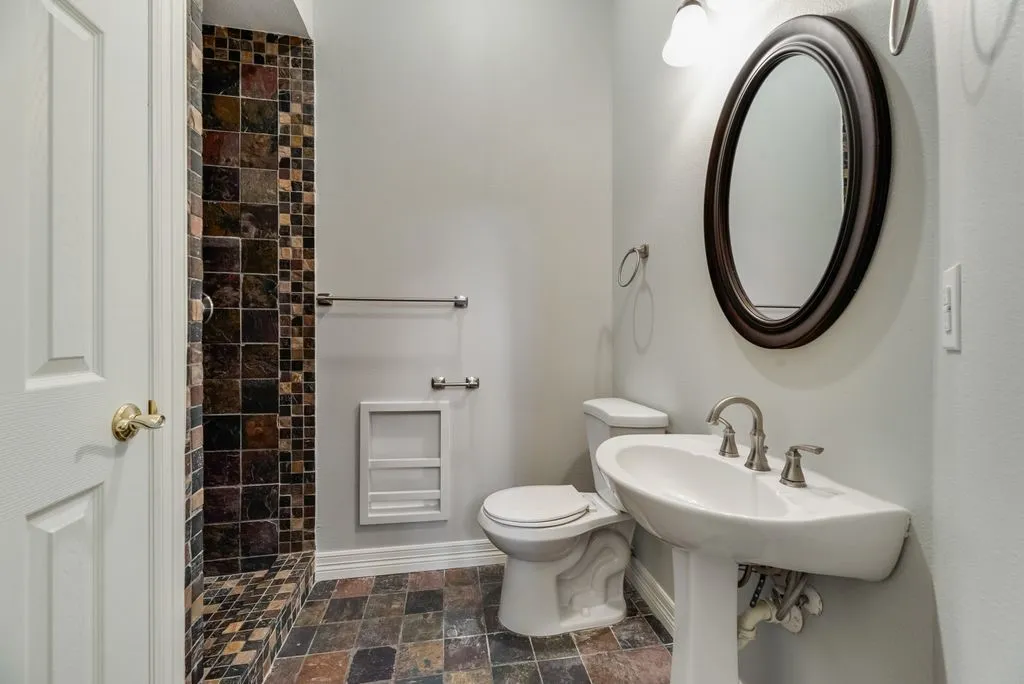 Bathroom featuring a pedestal sink, oval mirror, and a shower with multi-toned tile