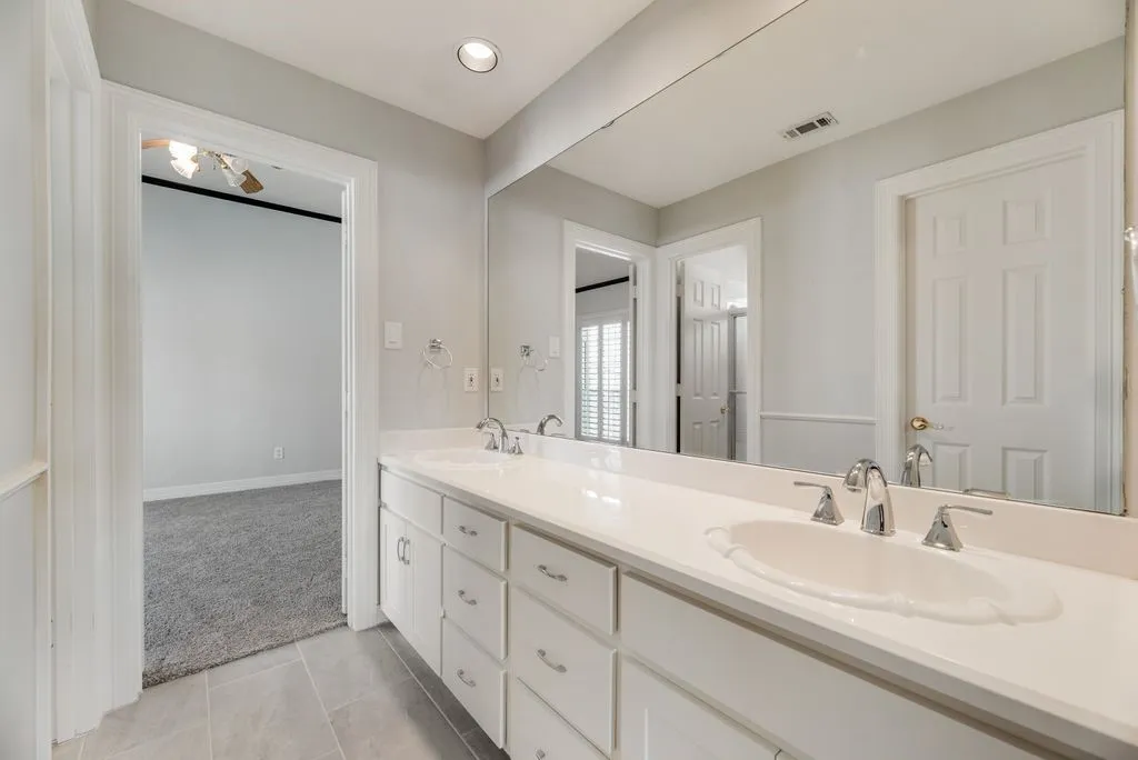 Bathroom vanity featuring a dual sink with polished chrome fixtures, a white solid surface countertop, and white cabinetry