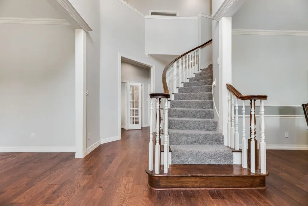Sweeping curved staircase with carpeted treads and a dark wood handrail, complemented by hardwood-finish flooring