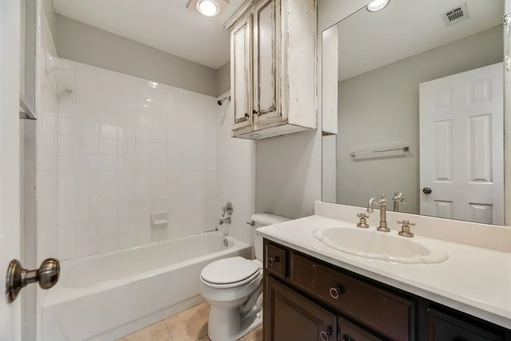 Bathroom featuring a built-in tub with white subway tile surround, a dark wood-finish vanity with a white countertop, an undermount sink with a brushed nickel faucet, and a wall-mounted mirror